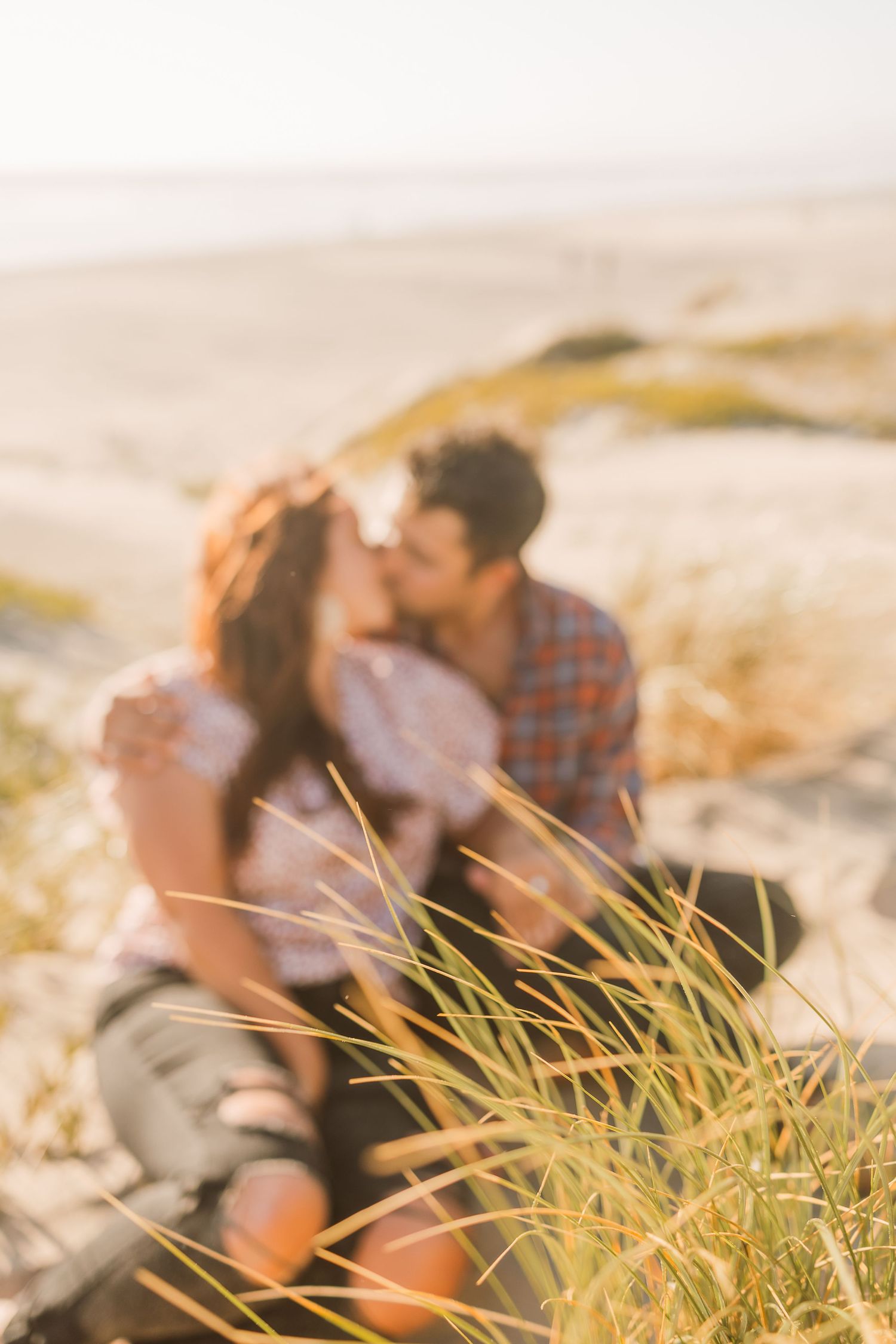 Couple sharing tender moment among beach grass during sunset.