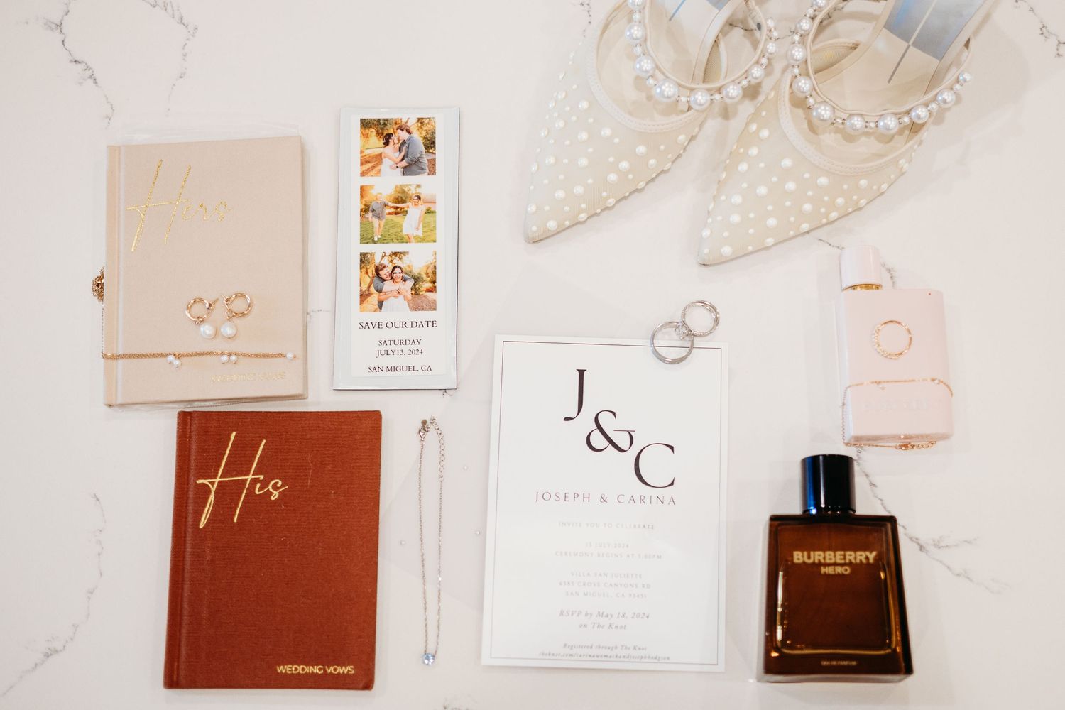 Wedding details flatlay with invitation cards, perfume bottle, rings, and embellished shoes on white background.