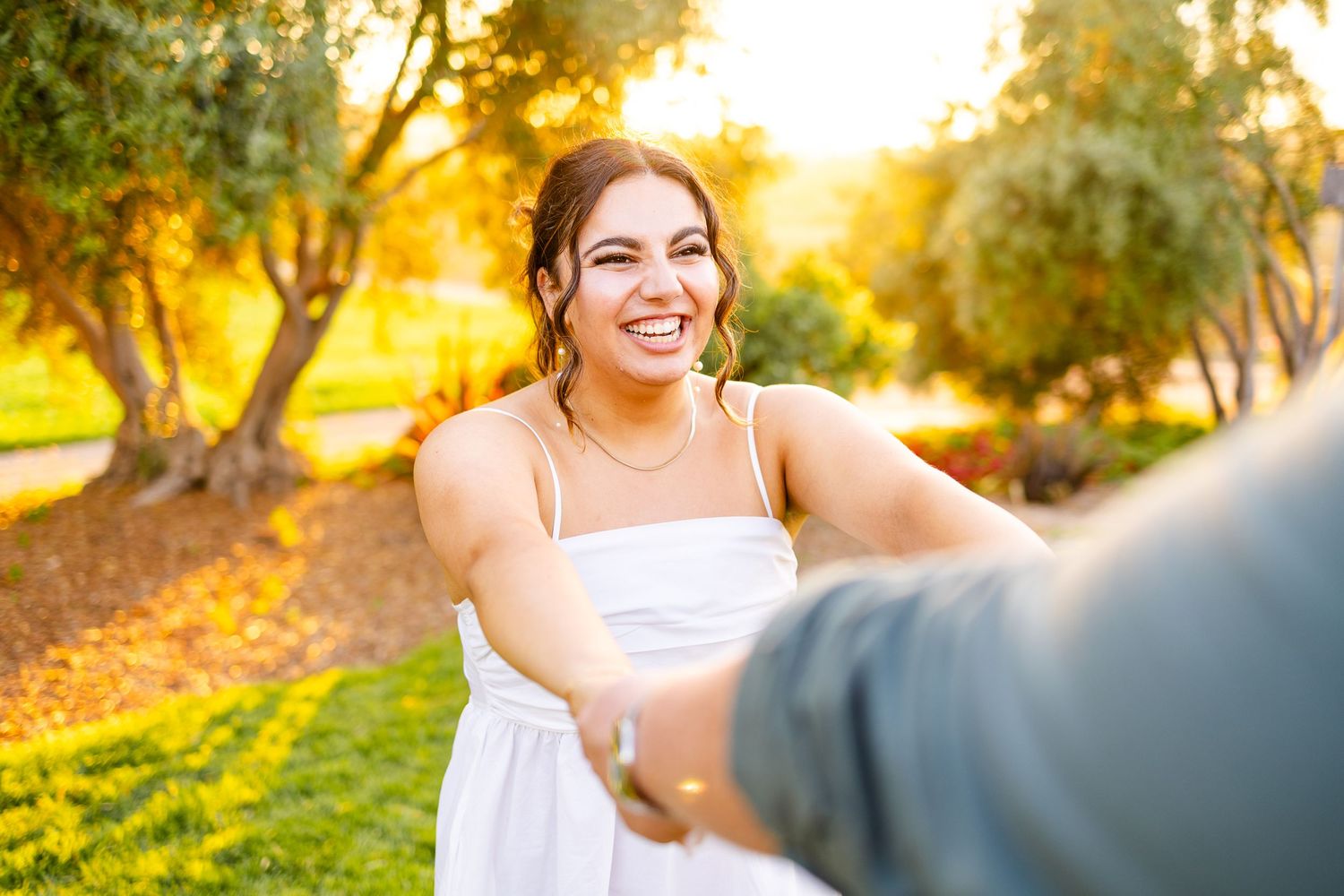 Couple shares a joyful moment outdoors during sunset in a garden setting.