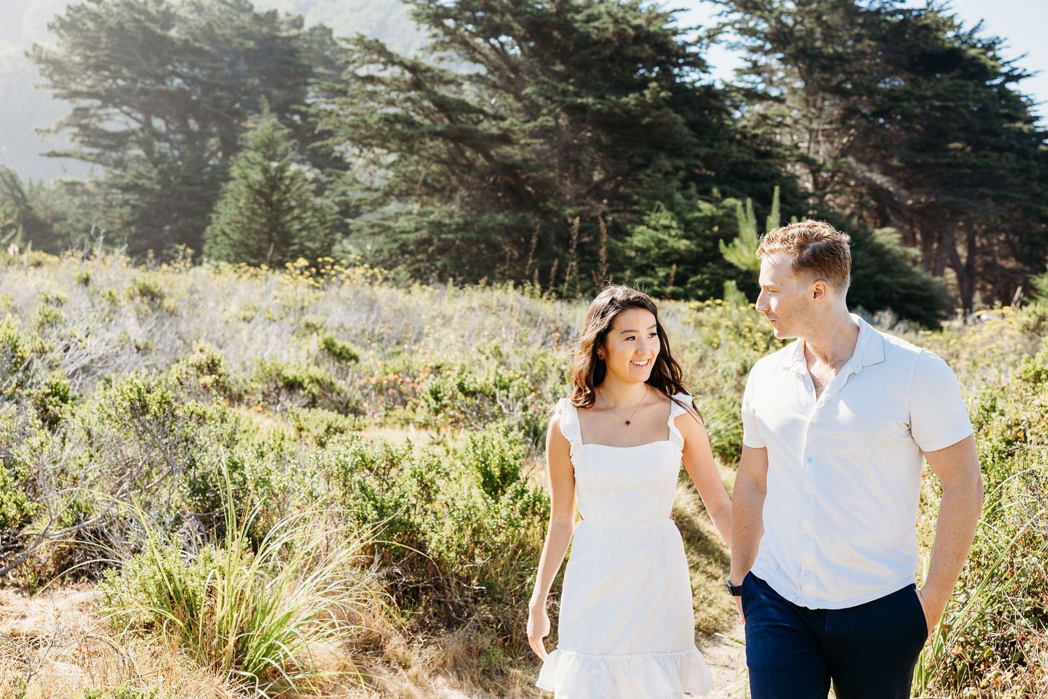 Sunny outdoor portrait of couple walking through wildflower meadow.
