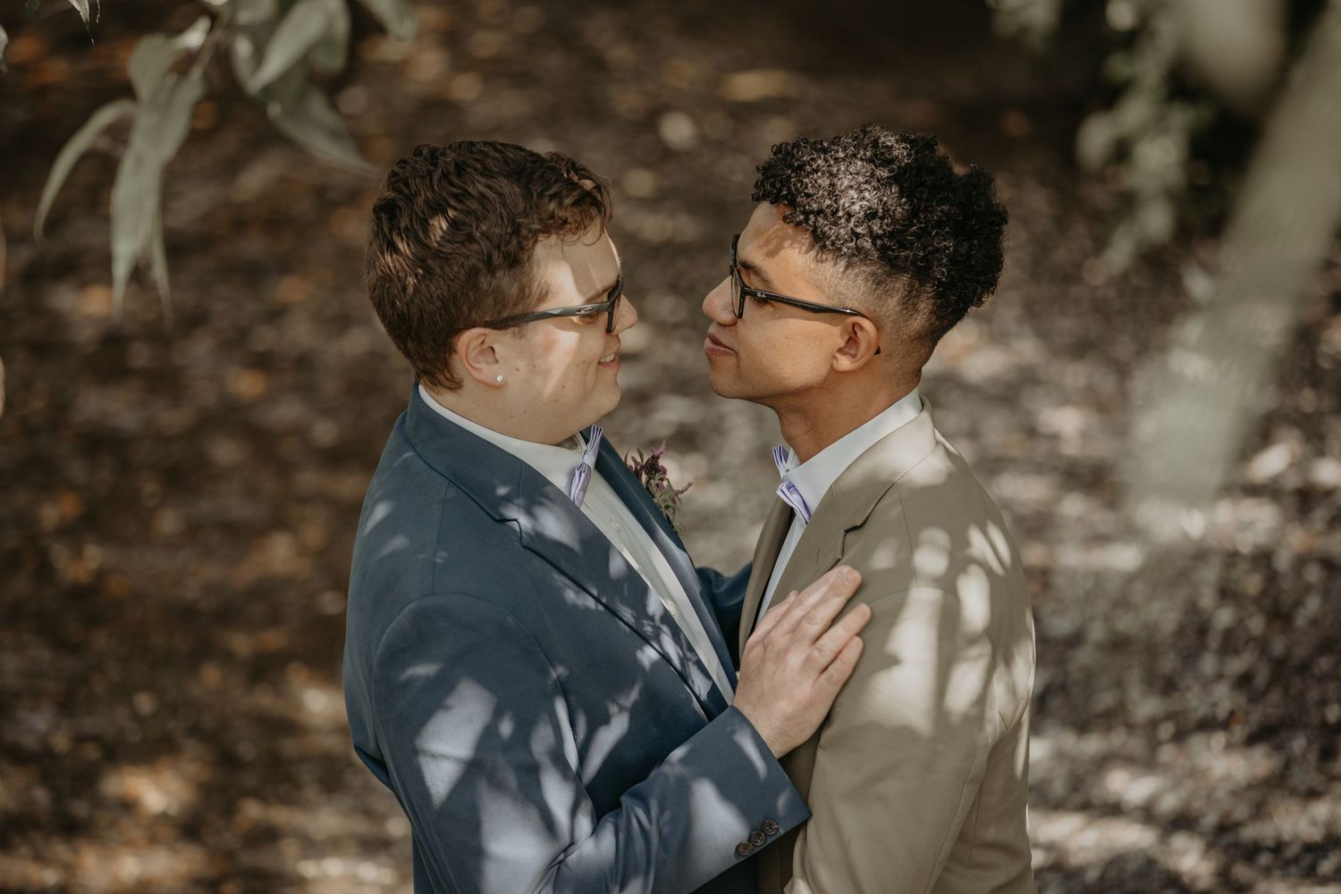 A couple wearing wedding attire shares romantic moments in a natural outdoor setting with dappled sunlight.