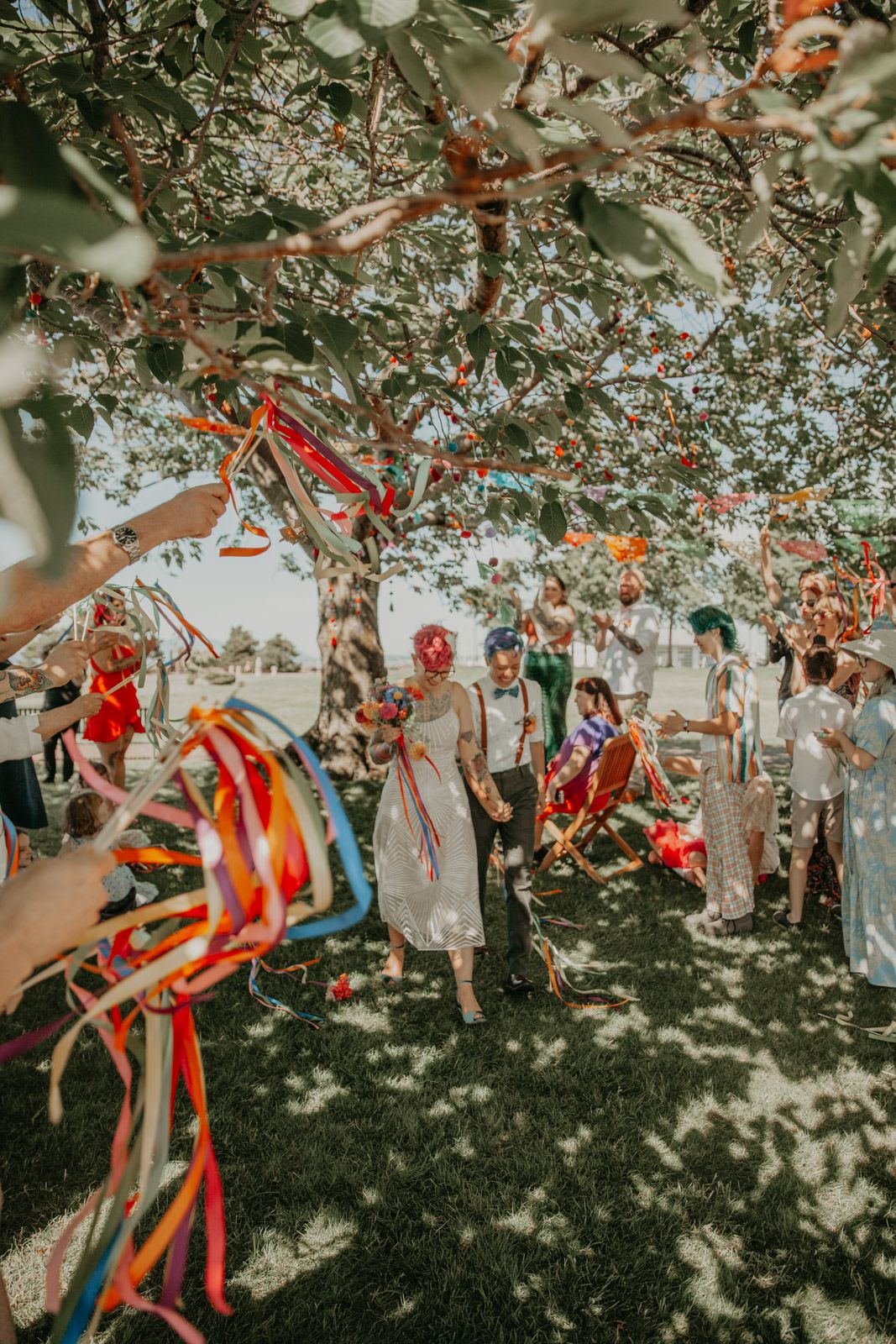 Colorful streamers and decorations hang from tree branches at outdoor celebration.