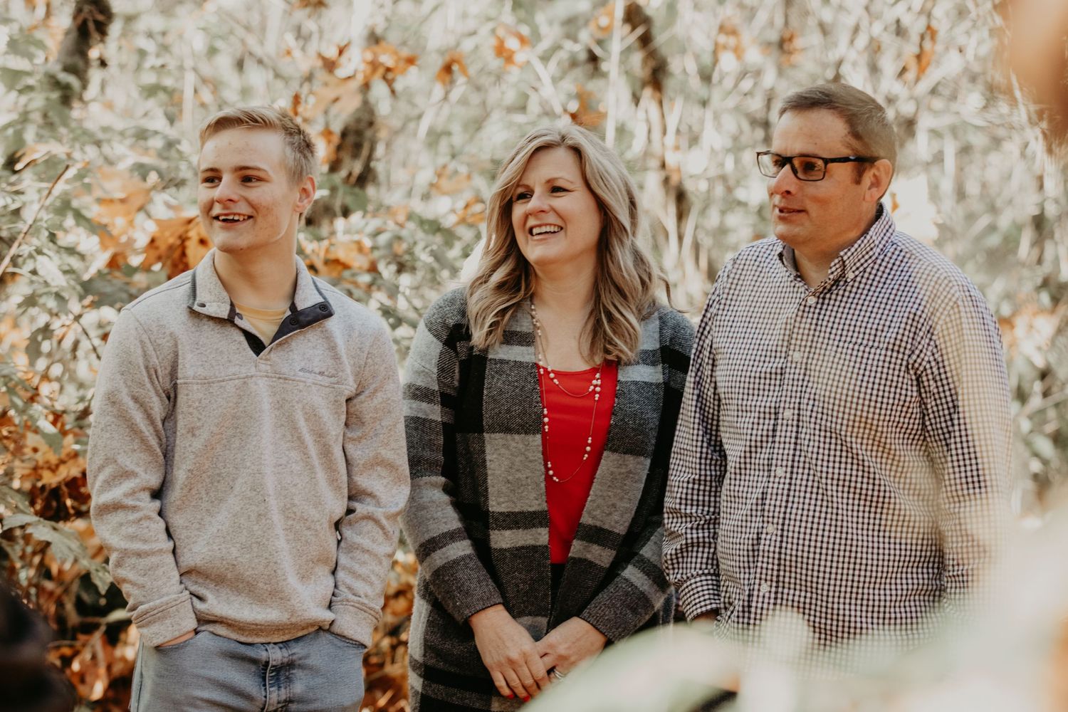 Three friends stand together outdoors in casual fall clothing against an autumn background with golden foliage.