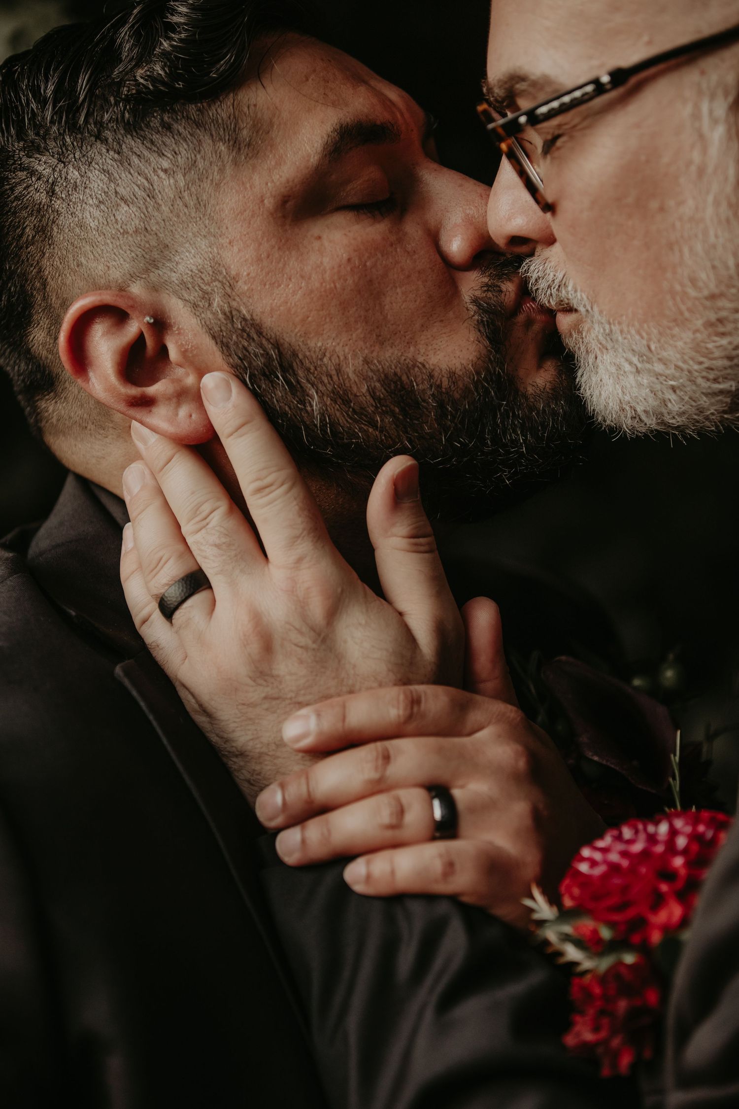Close up shot of two people sharing an intimate kiss with red flowers in frame.