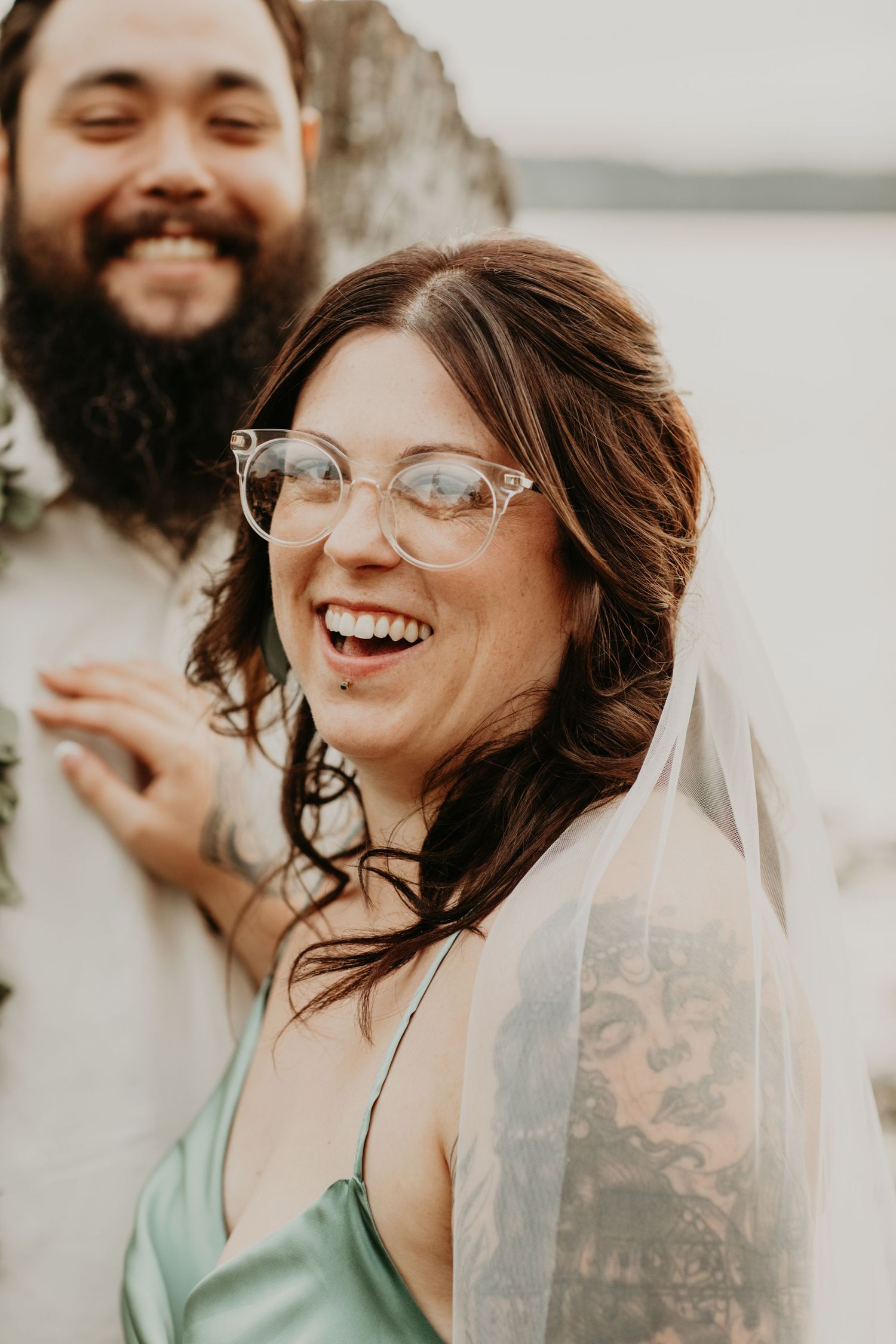 A happy couple shares a joyful moment outdoors, with a delicate veil and clear-framed glasses adding romantic details.
