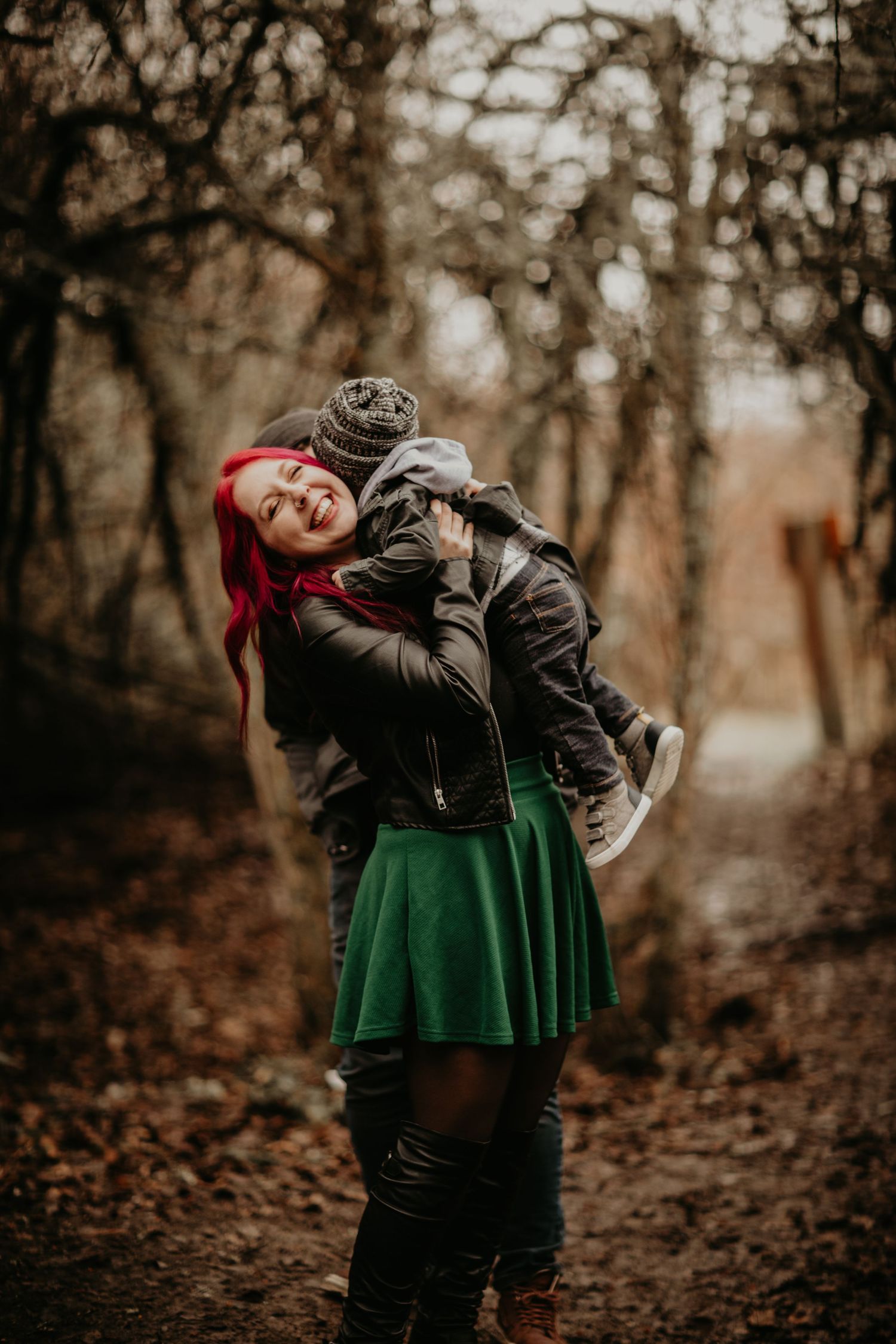 Figure in black jacket and emerald green skirt with bright red hair embraces warm autumn forest atmosphere nostalgically.