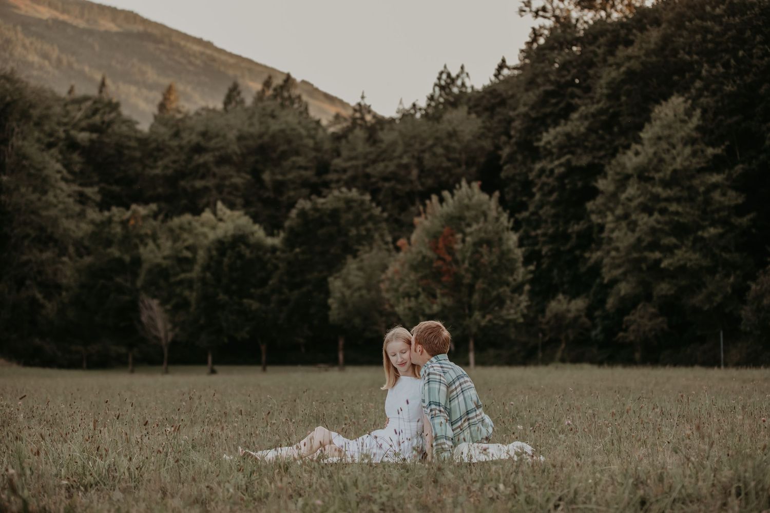 A couple shares an intimate moment while lying together in a serene meadow at sunset.