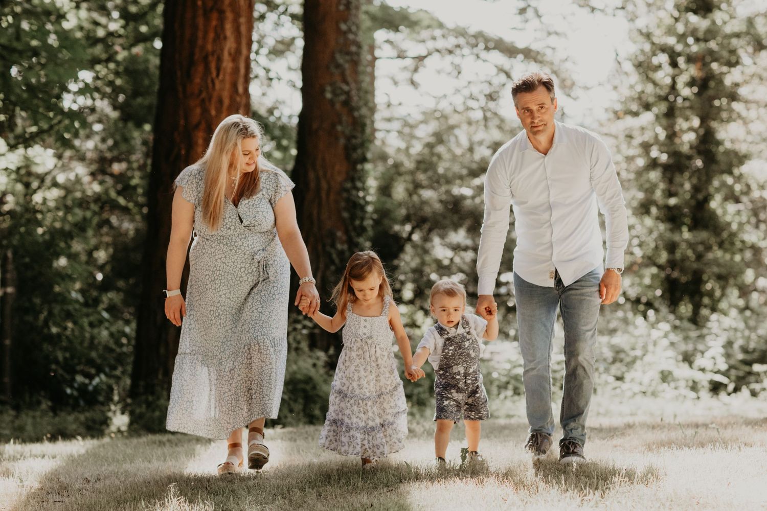 A family walks together on a sunlit forest path during a warm summer day in matching casual outfits.