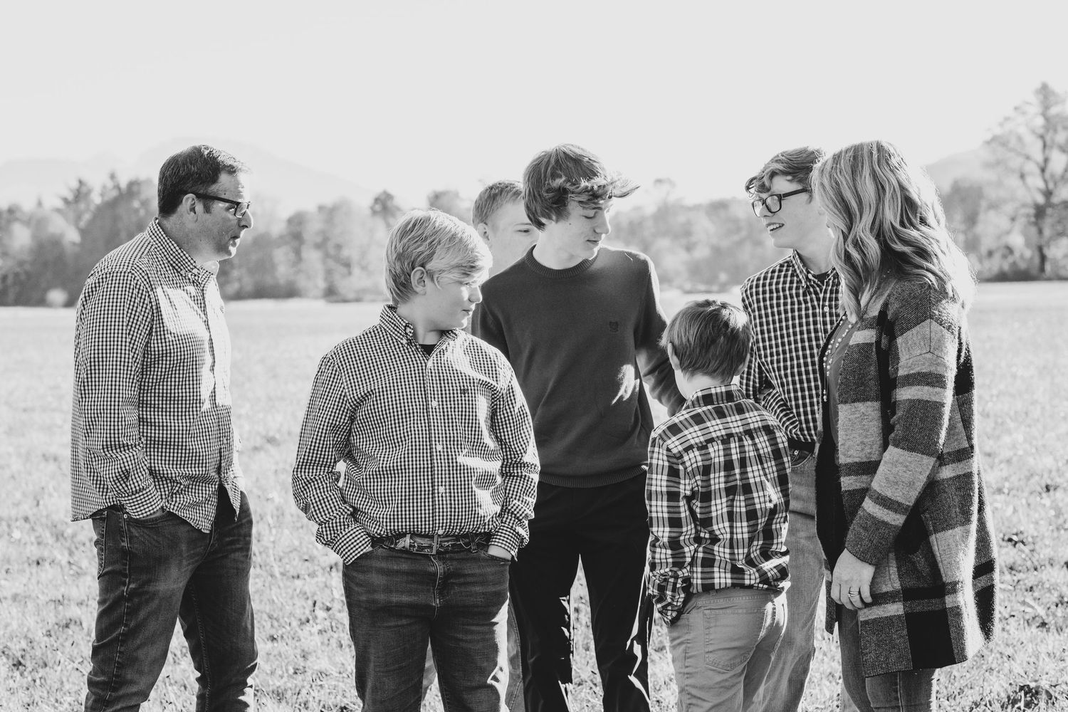 A group stands together in conversation, captured in black and white photography in an open field.
