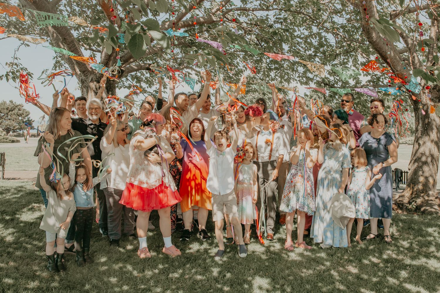 Large group gathers under decorated trees for outdoor celebration.