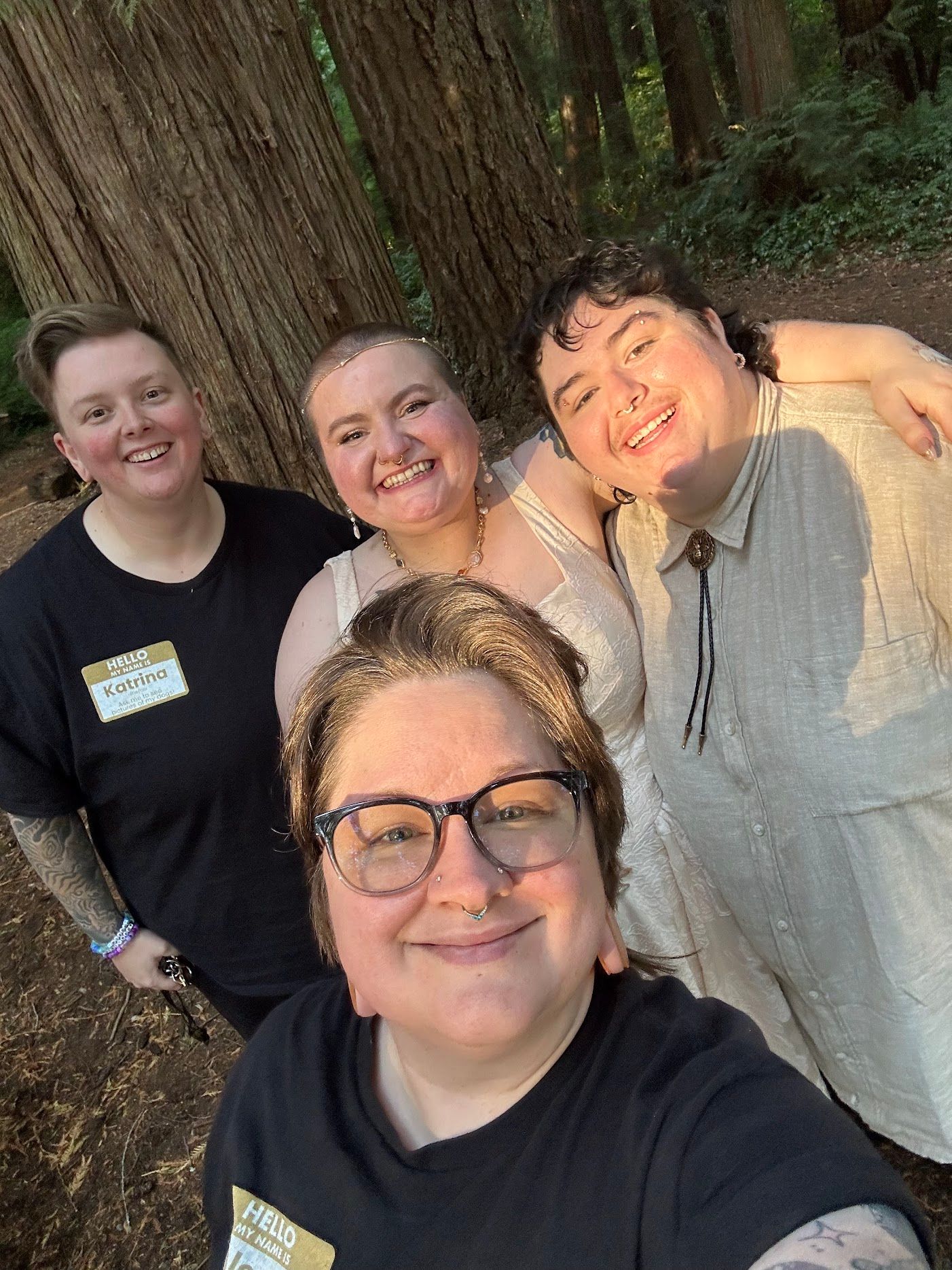 A group of people taking a selfie together in front of a large redwood tree trunk in a forest setting.