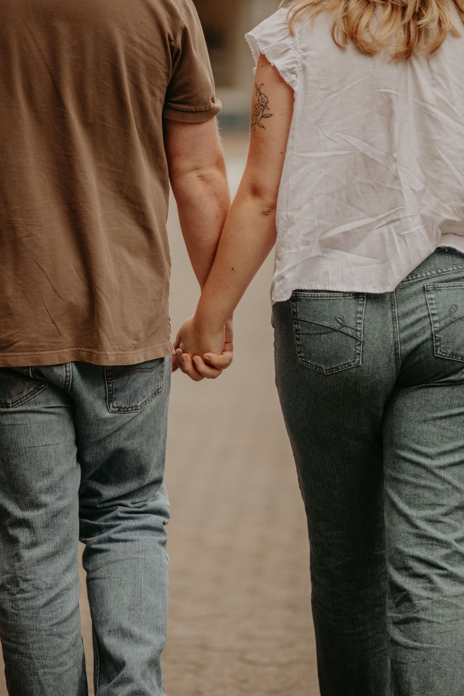 Close-up view of a couple holding hands while wearing blue jeans and casual clothing in natural light.