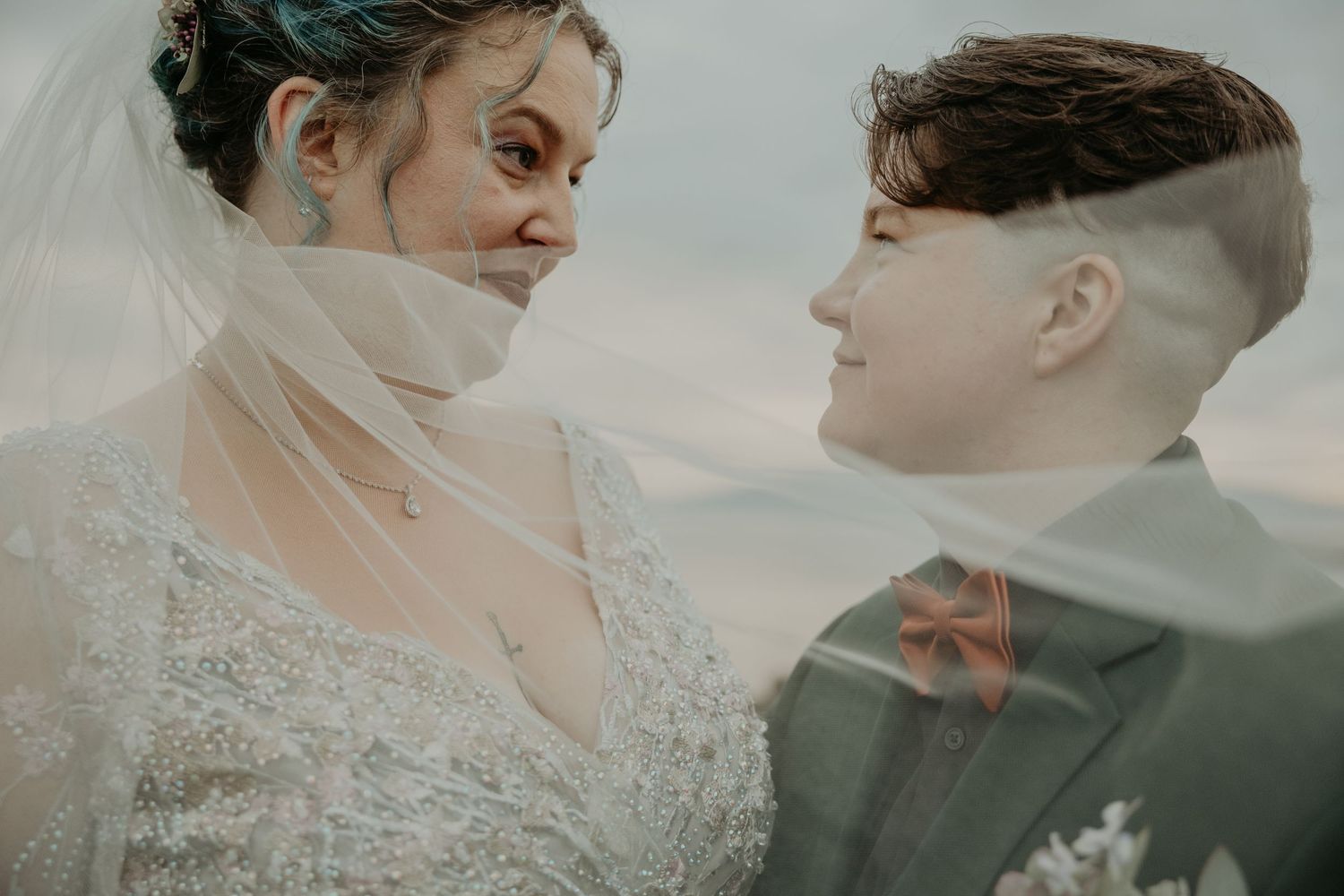 A couple shares an intimate moment in formal wedding attire against a soft, romantic backdrop.