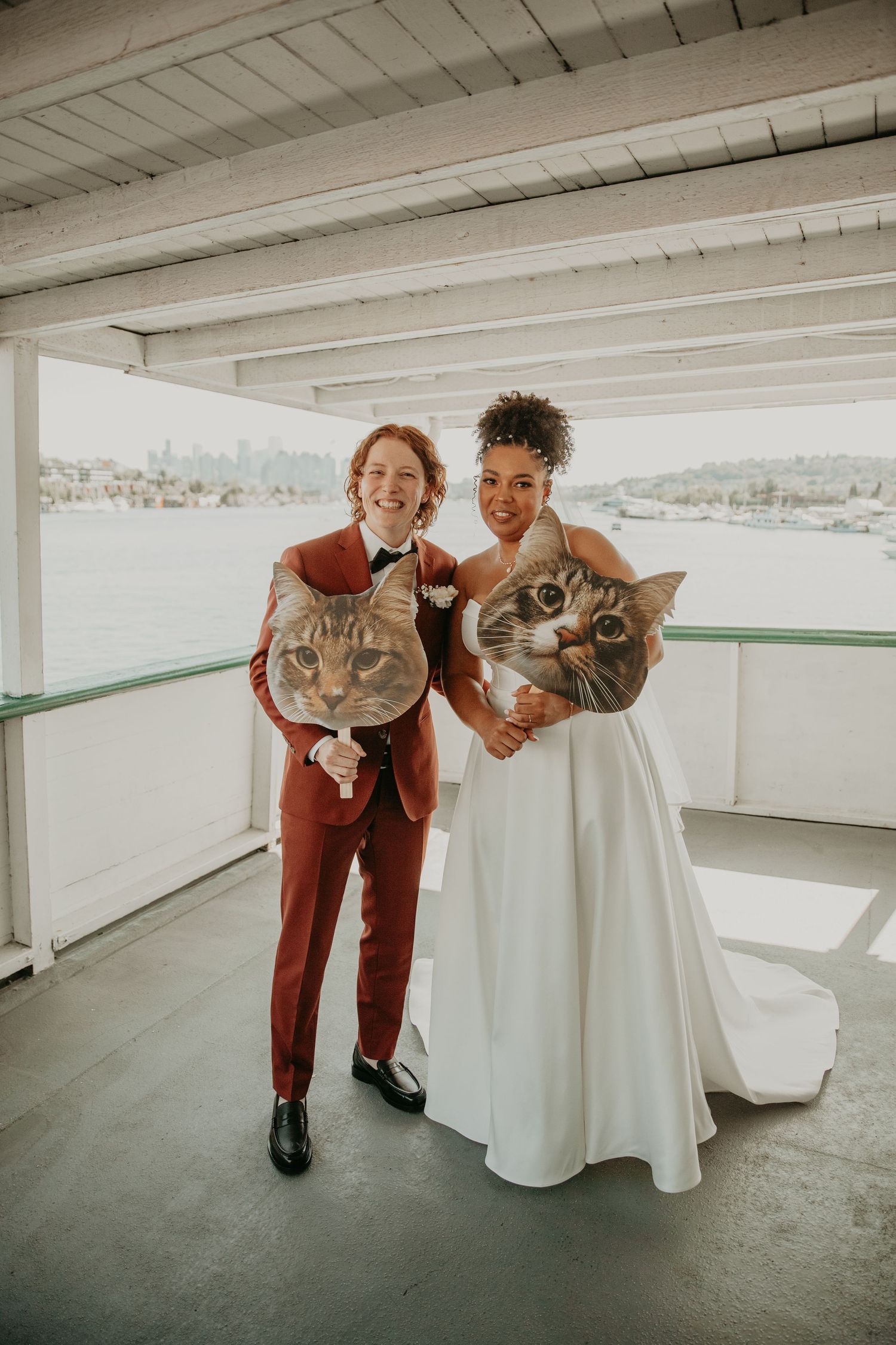 Couple in burgundy suit and white dress playfully pose together in a parking garage setting.