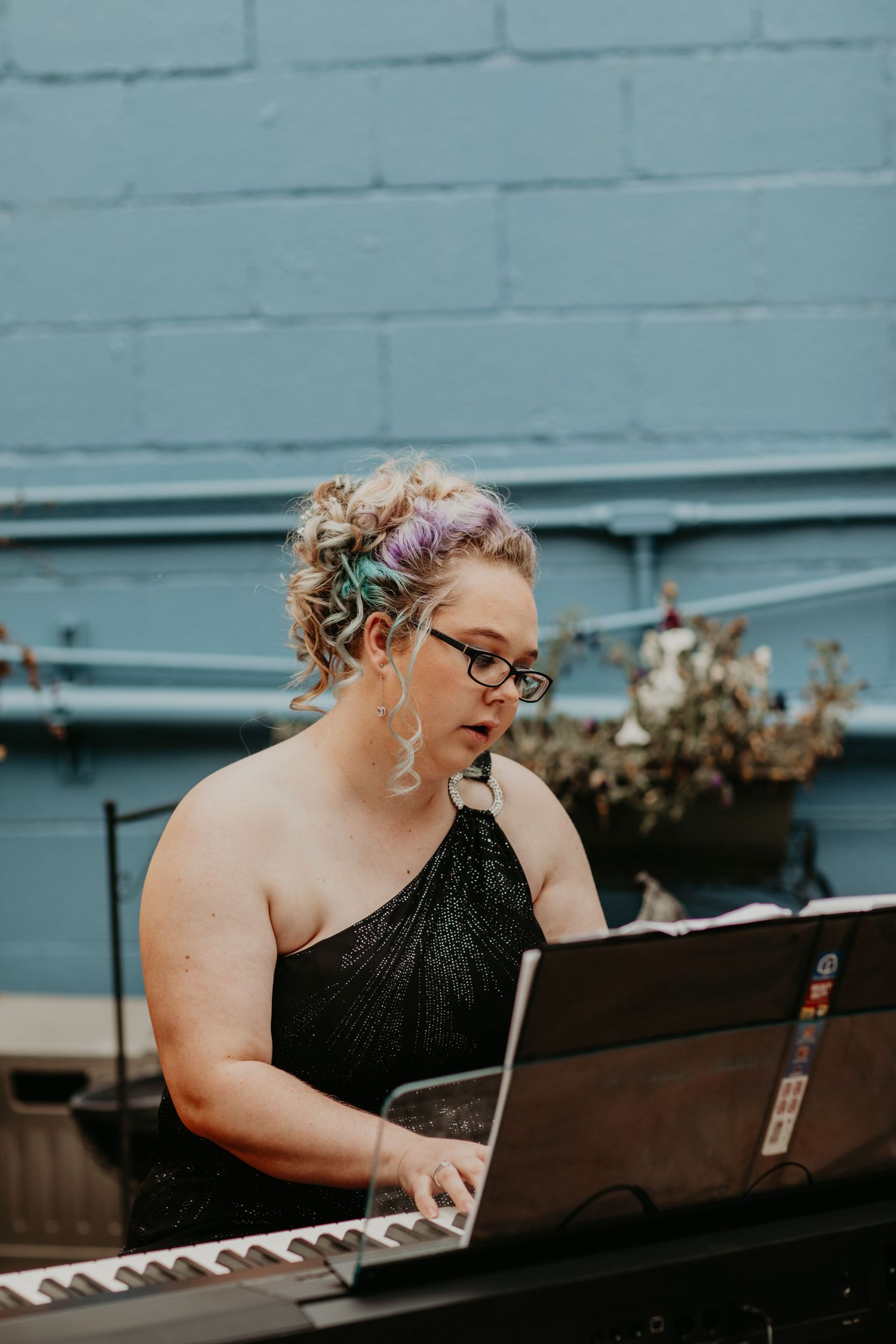 Pianist wearing glasses and formal black dress performs with sheet music at outdoor venue.