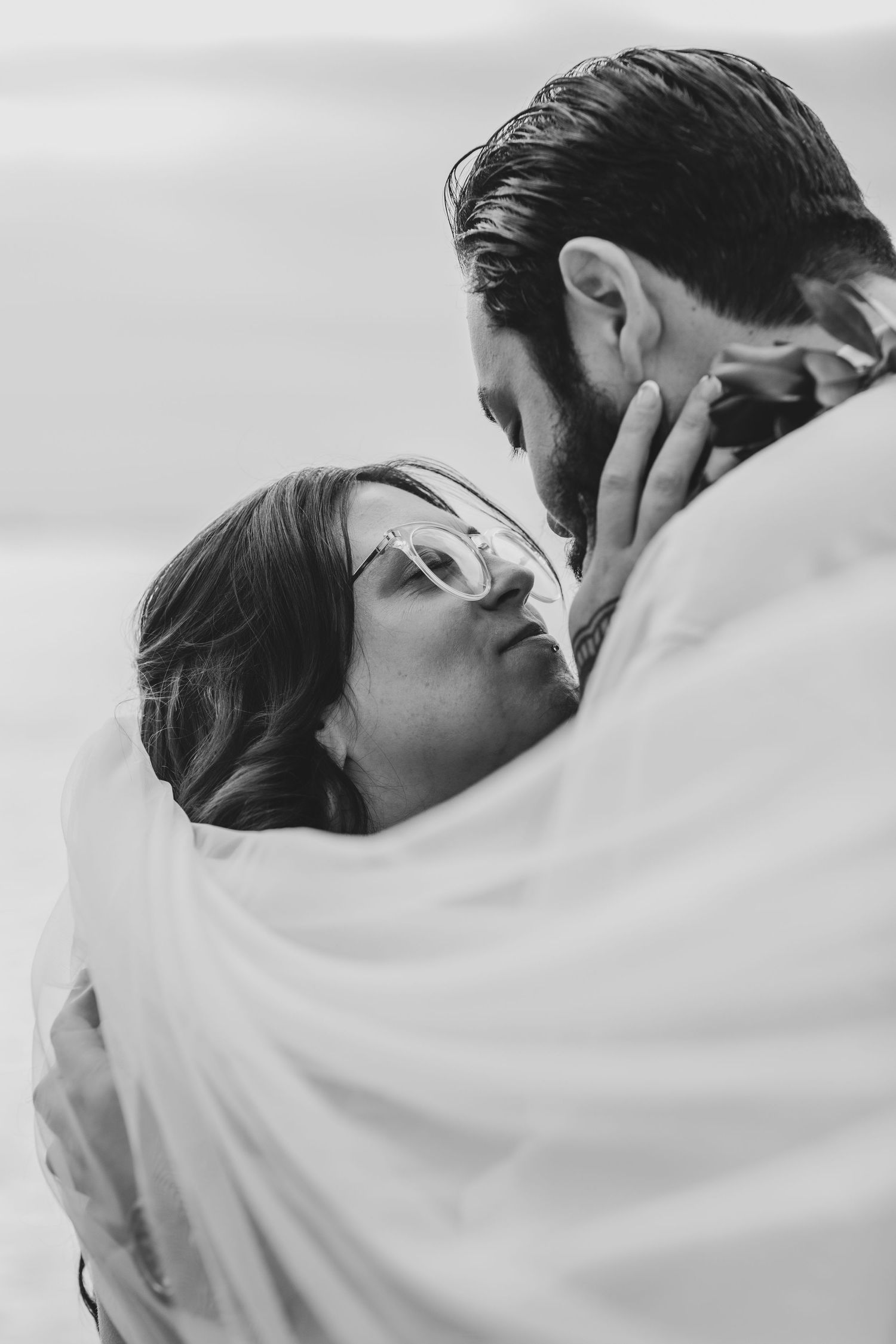 A romantic black and white photo of newlyweds sharing an intimate moment under a veil.