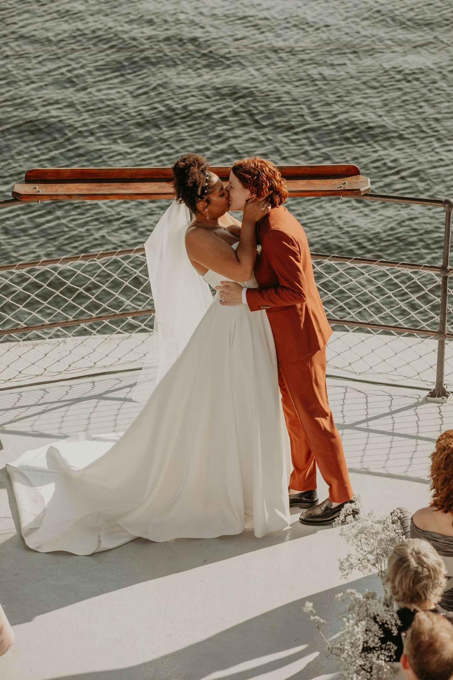 Wedding couple posing on a boat deck with white railings during sunset.