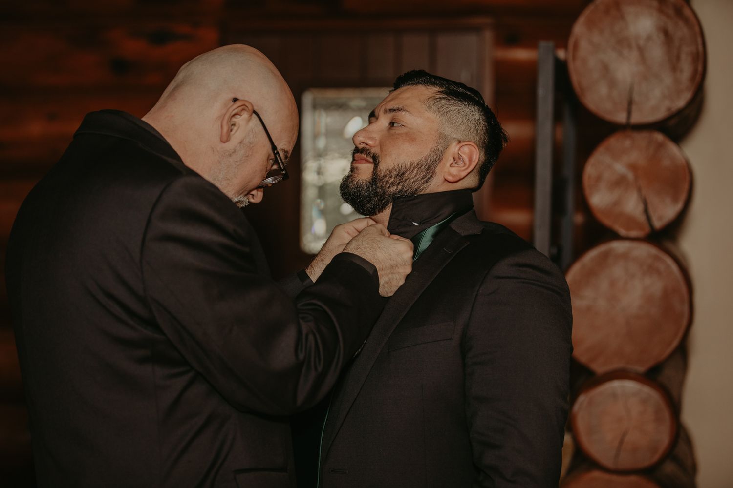 A couple embraces intimately in a dimly lit room with warm lighting and wooden accents in the background.
