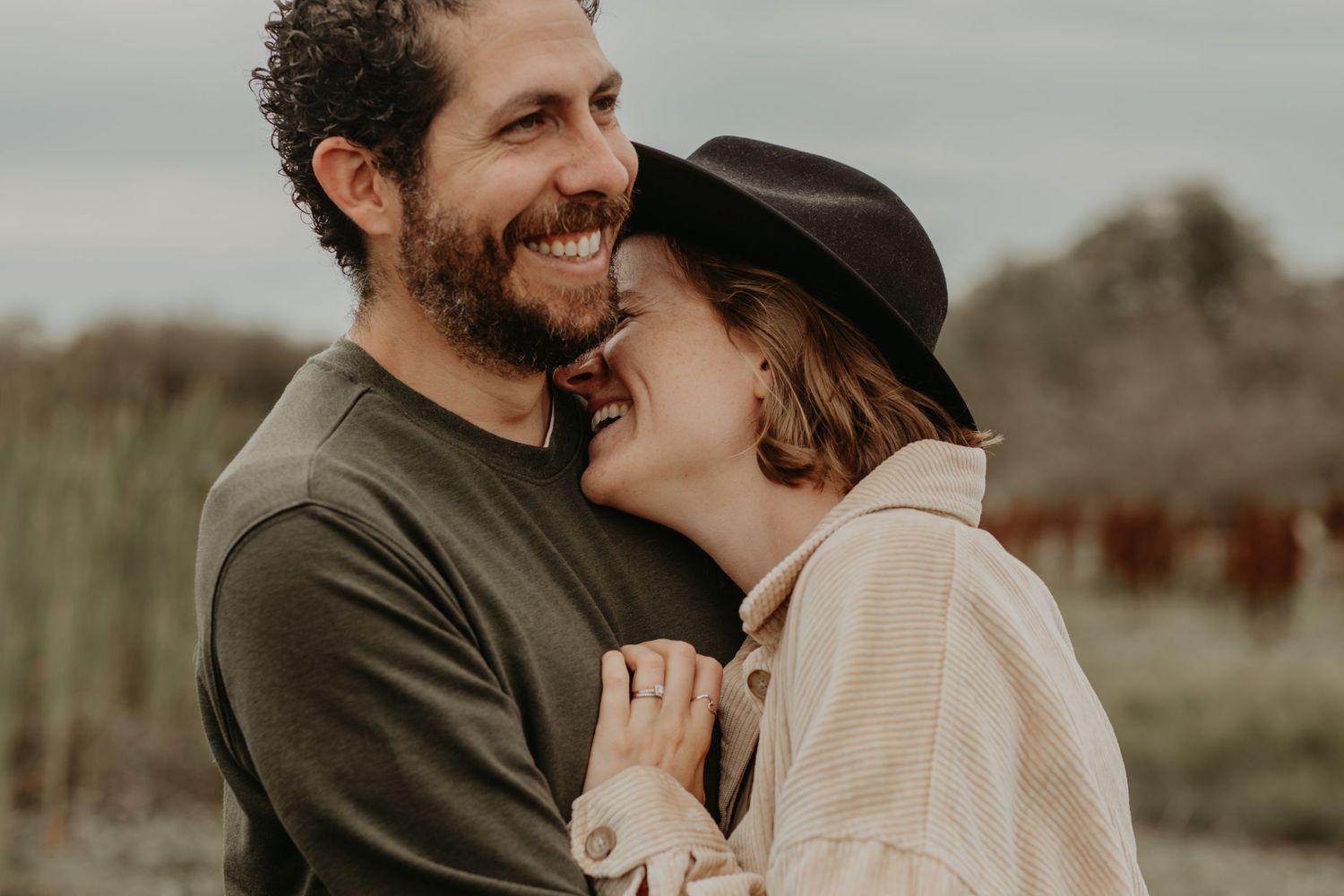 A romantic couple sharing an intimate moment outdoors, with one wearing a dark hat and the other in olive green.