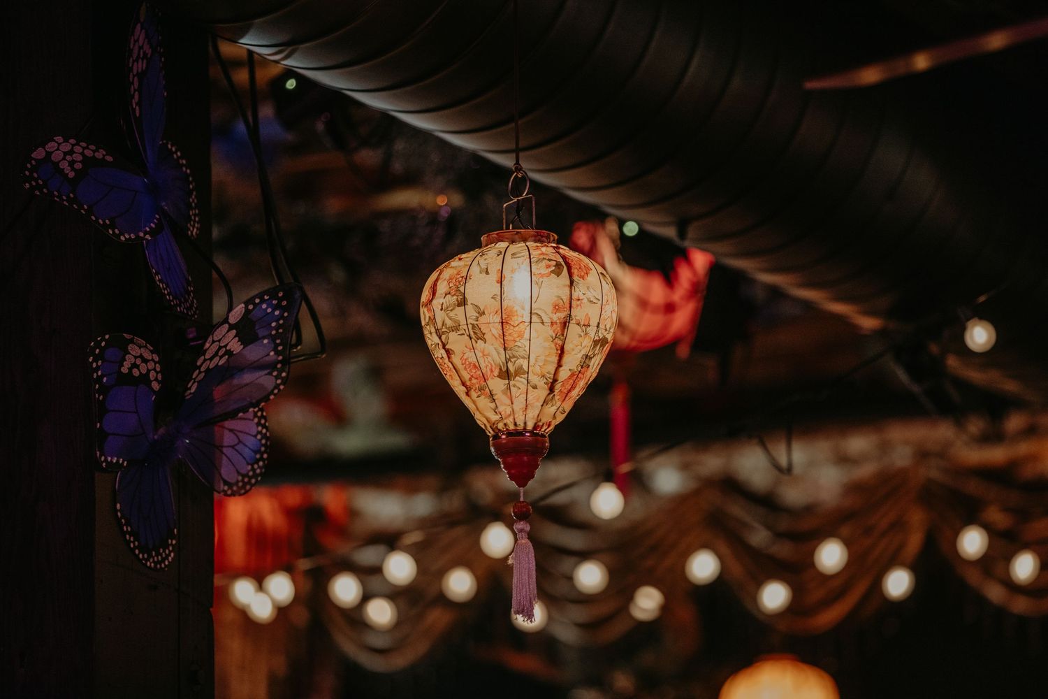 A glowing traditional Asian paper lantern hangs against a dark background with string lights creating a magical atmosphere.