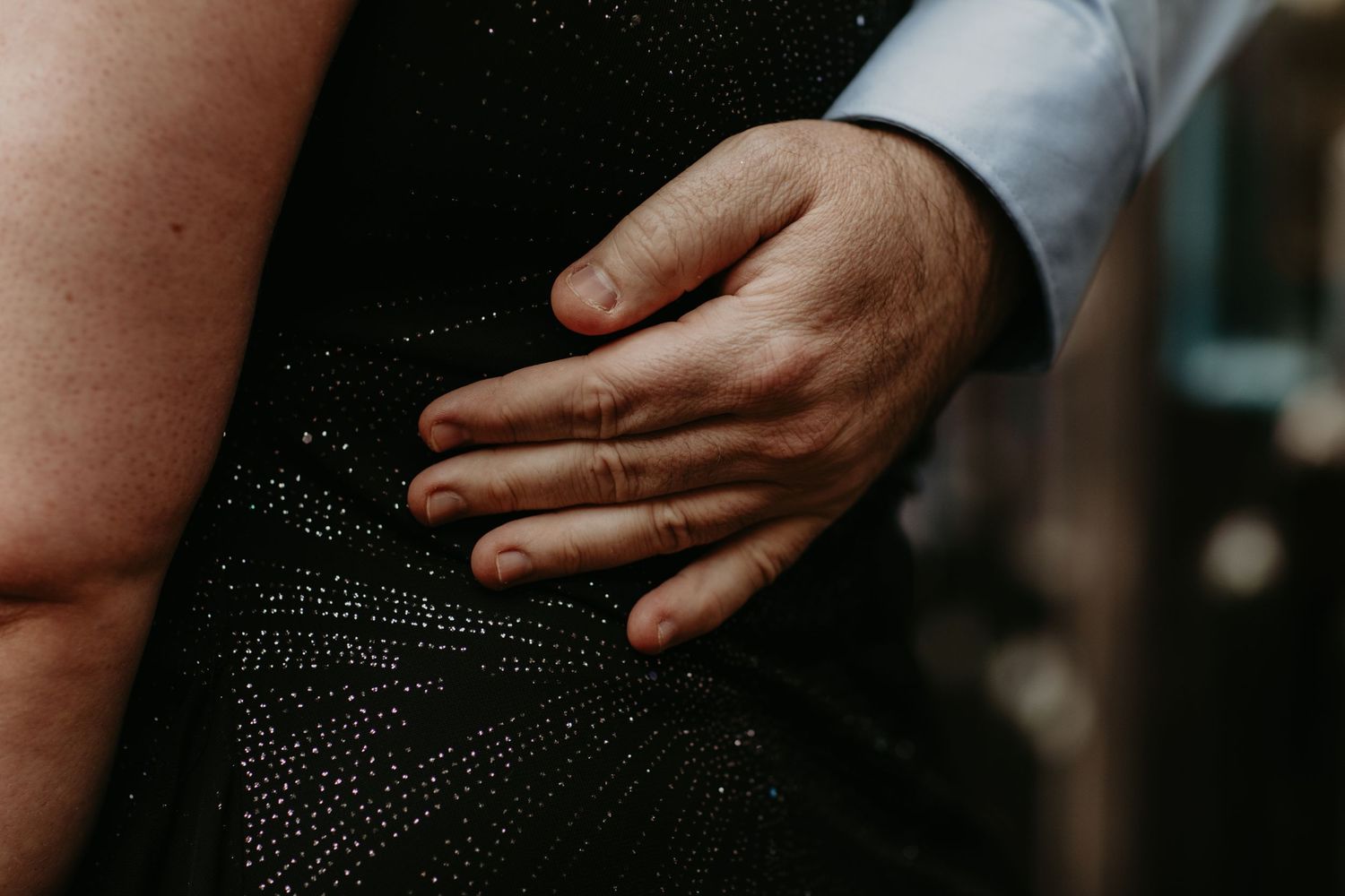 Close-up of a hand with a wedding ring resting on a black sequined dress fabric.