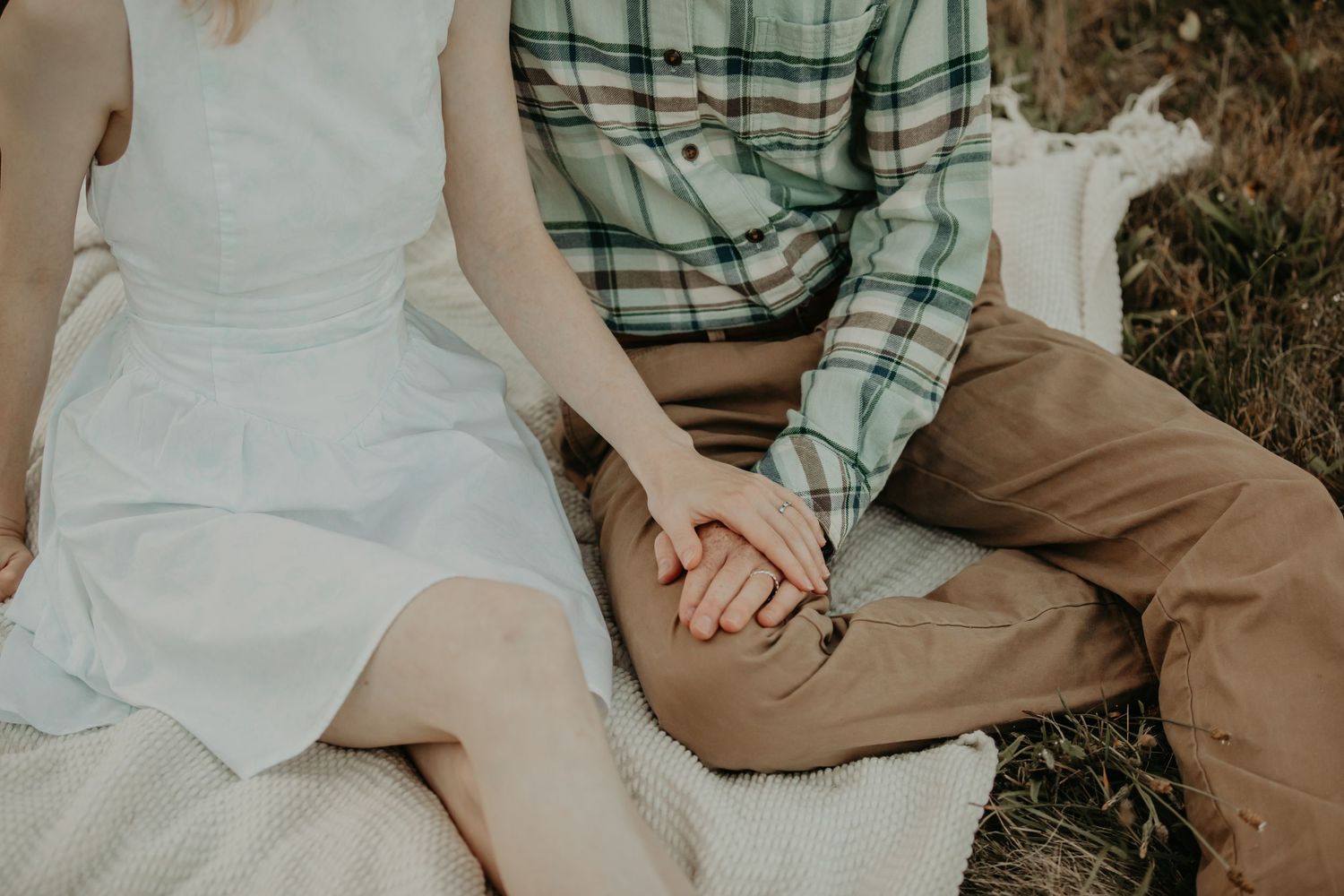 A couple sits close together outdoors in casual attire during a romantic engagement photo session.