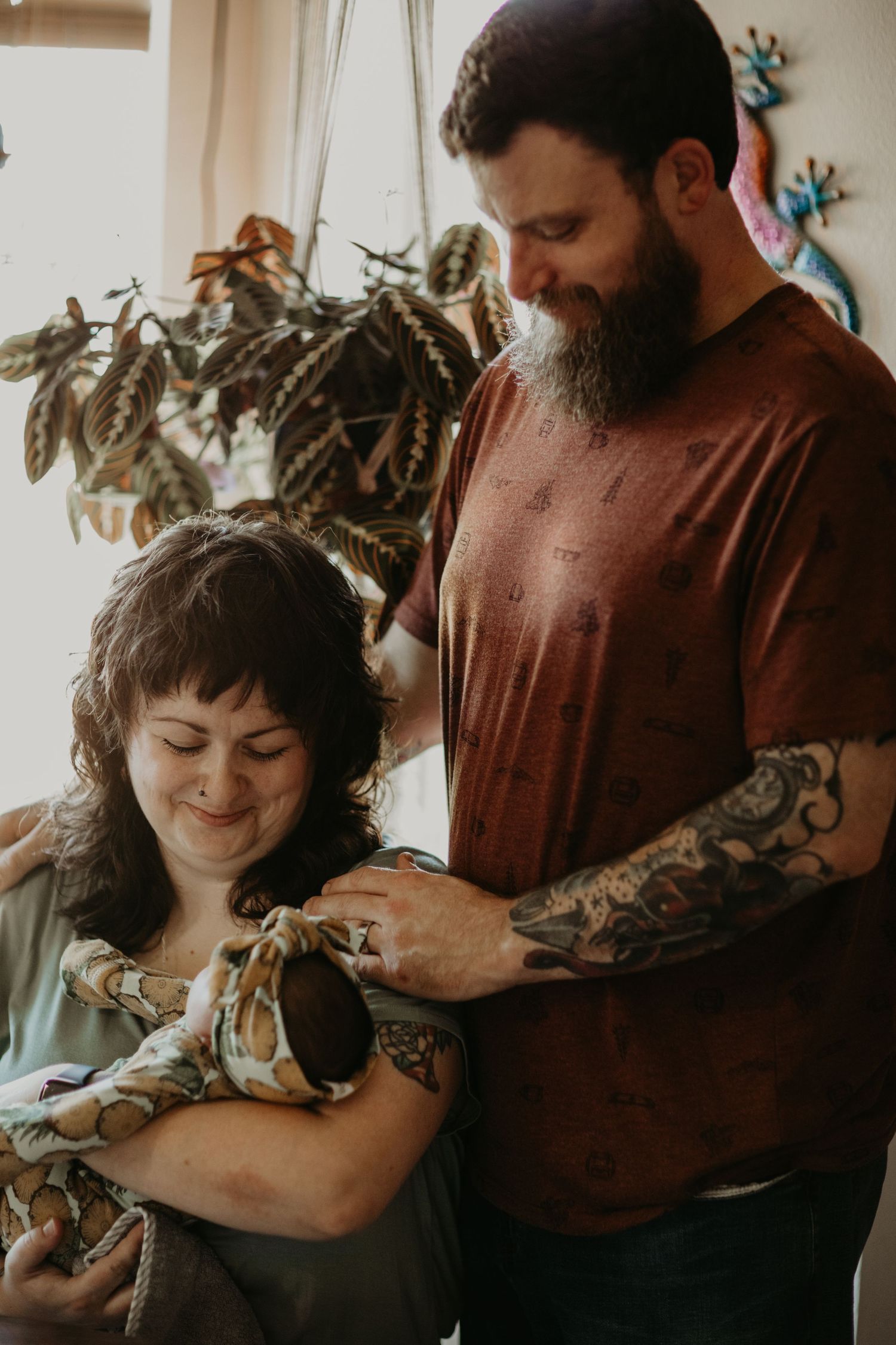 A tender family moment captured indoors showing a couple lovingly holding their newborn baby next to a houseplant.