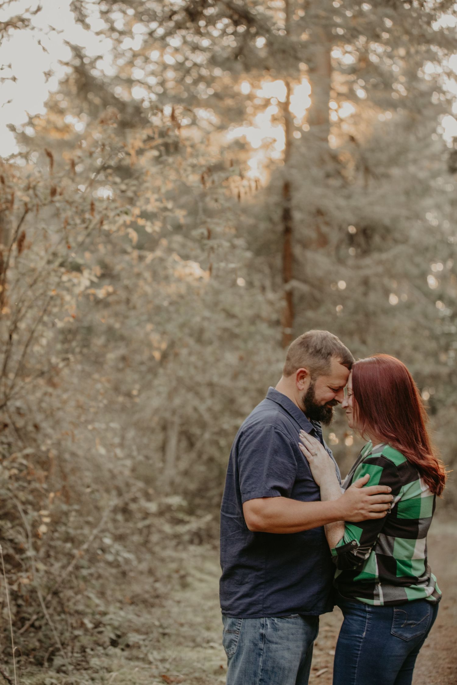 Intimate autumn forest engagement photo with couple embracing in a romantic moment at sunset.