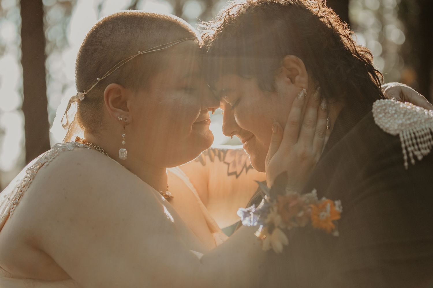 A romantic couple in warm sunlight share an intimate moment during their wedding photoshoot outdoors.
