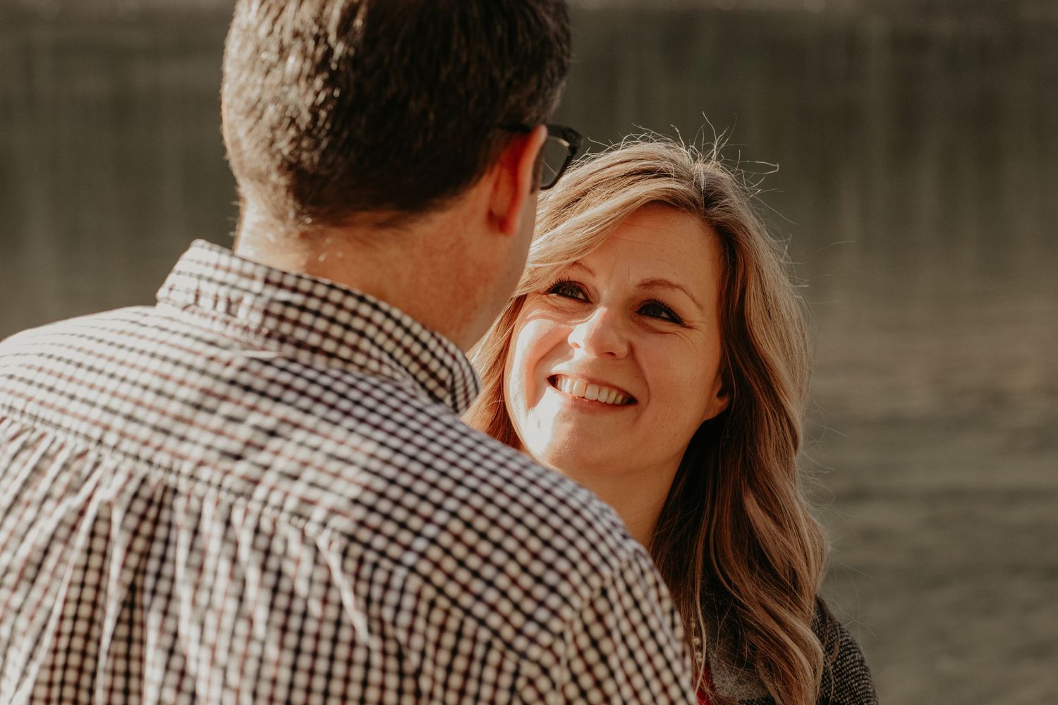 Two people share an intimate moment during an outdoor engagement photo session near water with warm lighting.