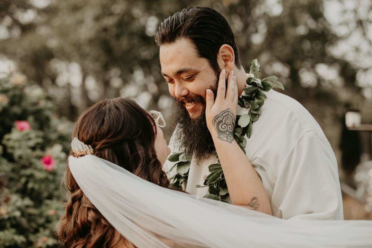 A couple shares an intimate moment during their Hawaiian wedding ceremony with traditional leis and a flowing veil.