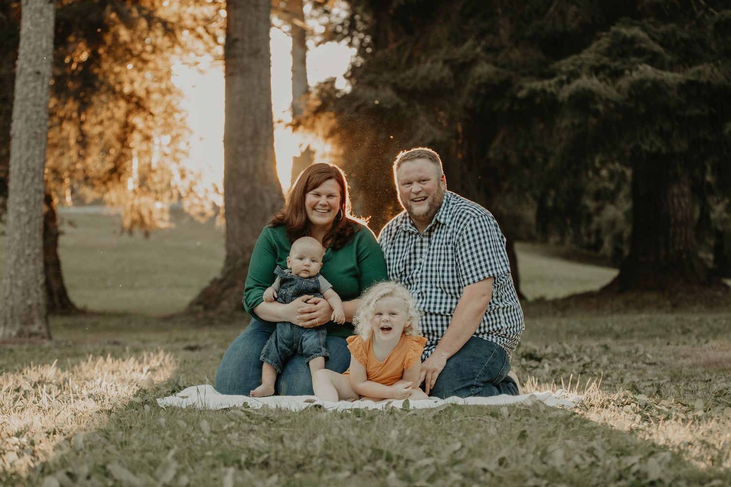 Family relaxing together on grass during golden hour sunset in park setting.