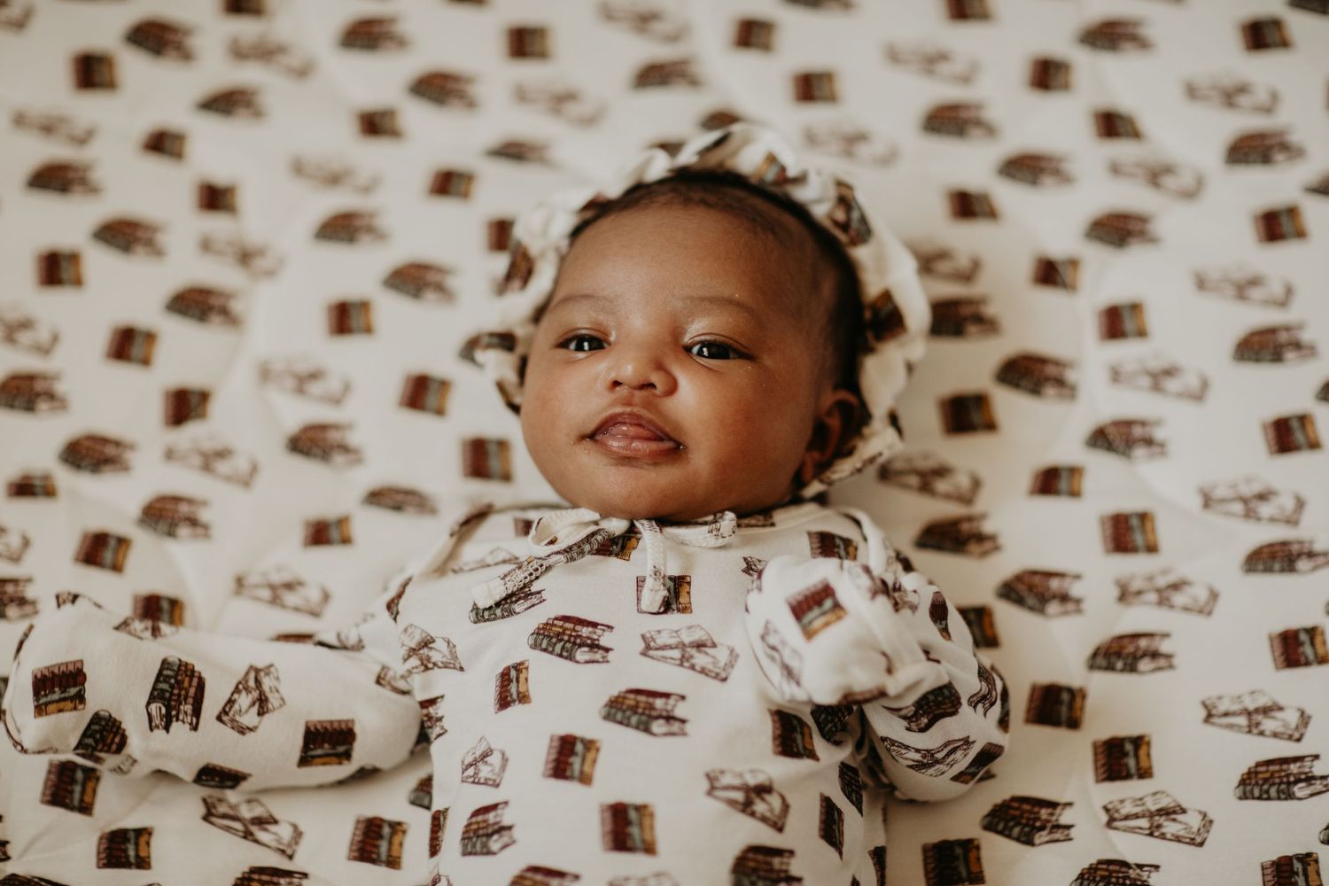 Sweet baby lying on patterned bedding wearing a white outfit with brown print design.