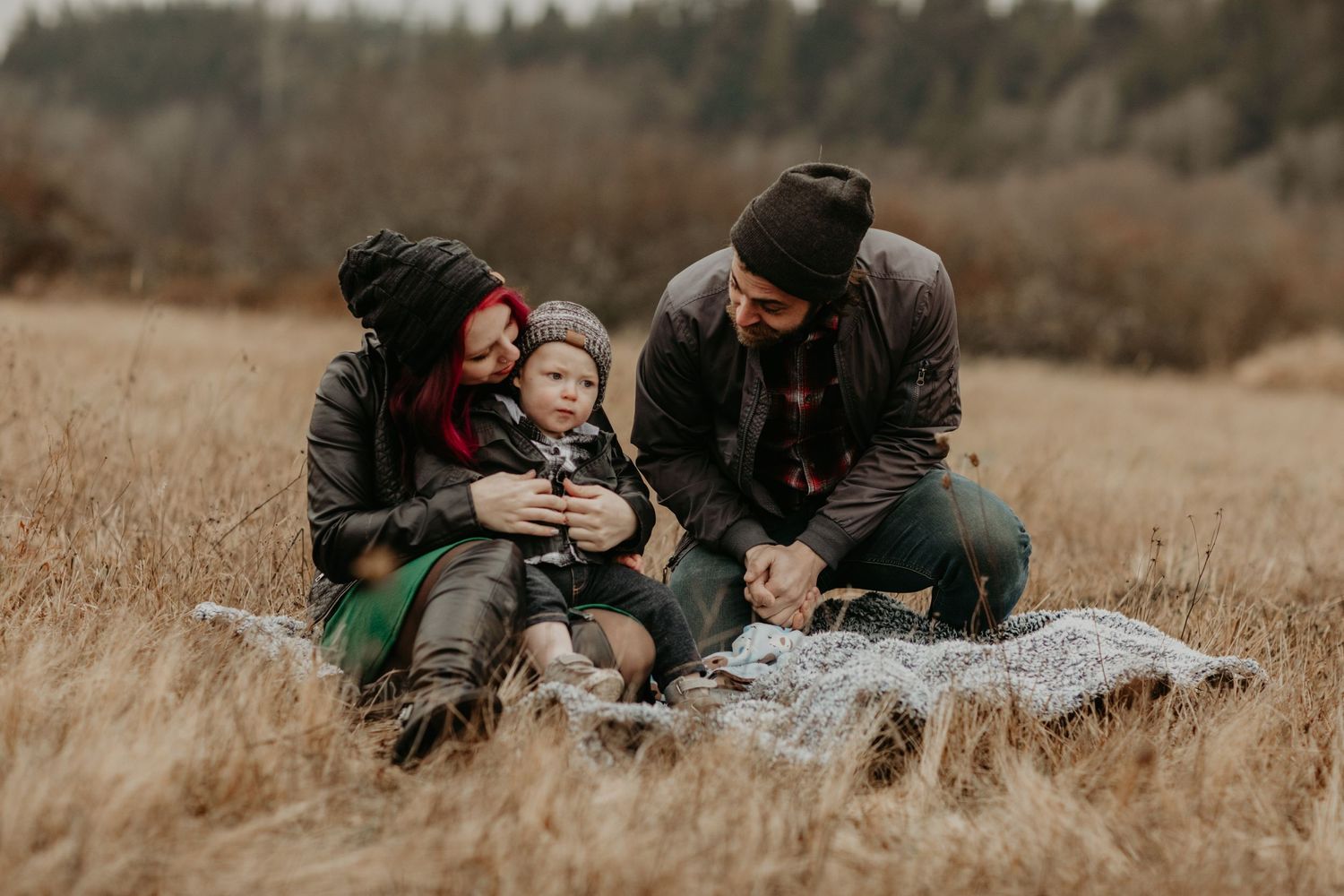 A couple sitting on a blanket in a golden autumn field with their dog while enjoying the outdoors together.