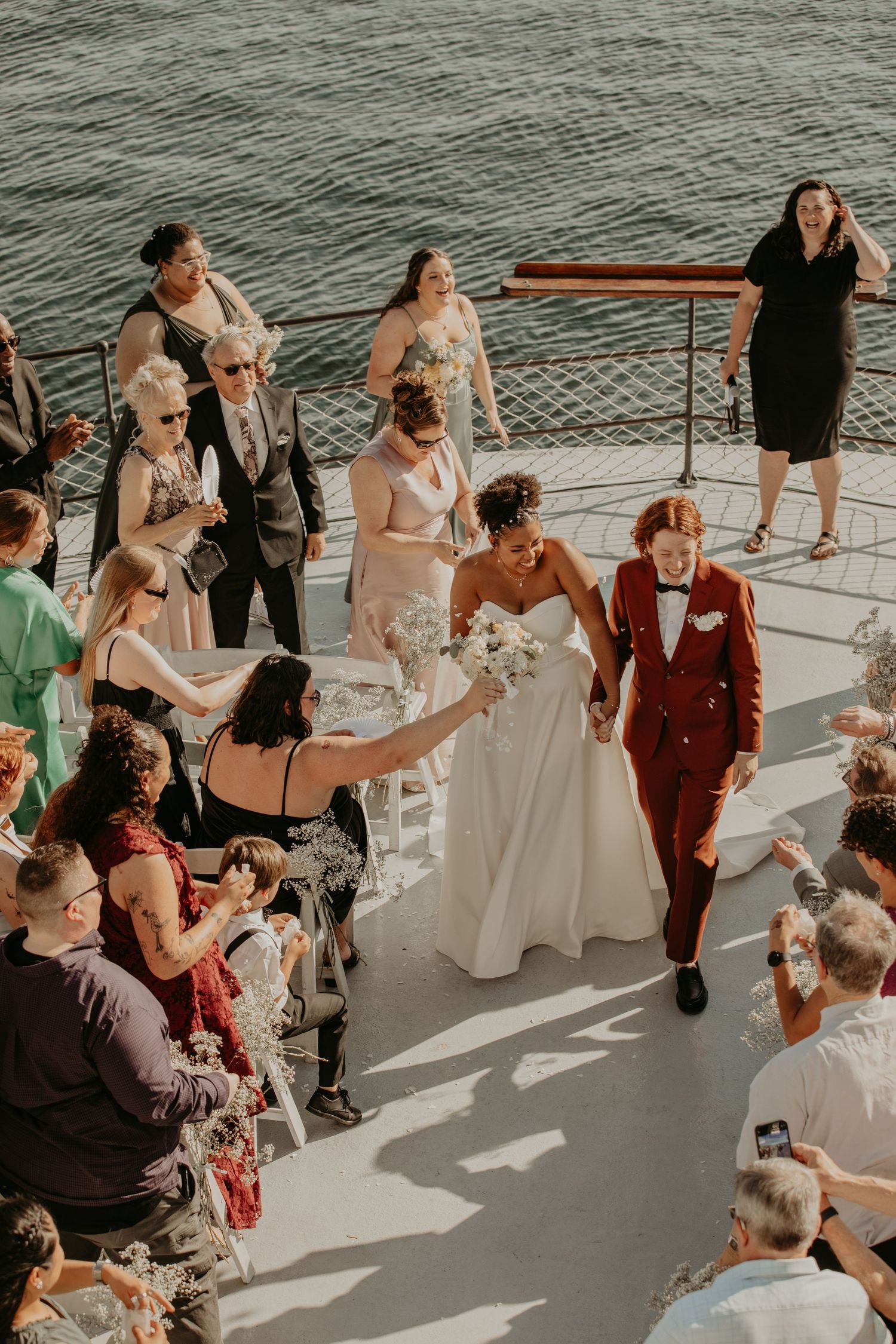 Wedding guests gather on a boat deck by the water during a nautical celebration on a sunny day.