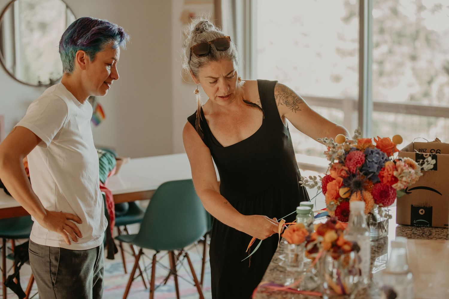 People arranging colorful floral centerpieces on wooden tables for an indoor event.