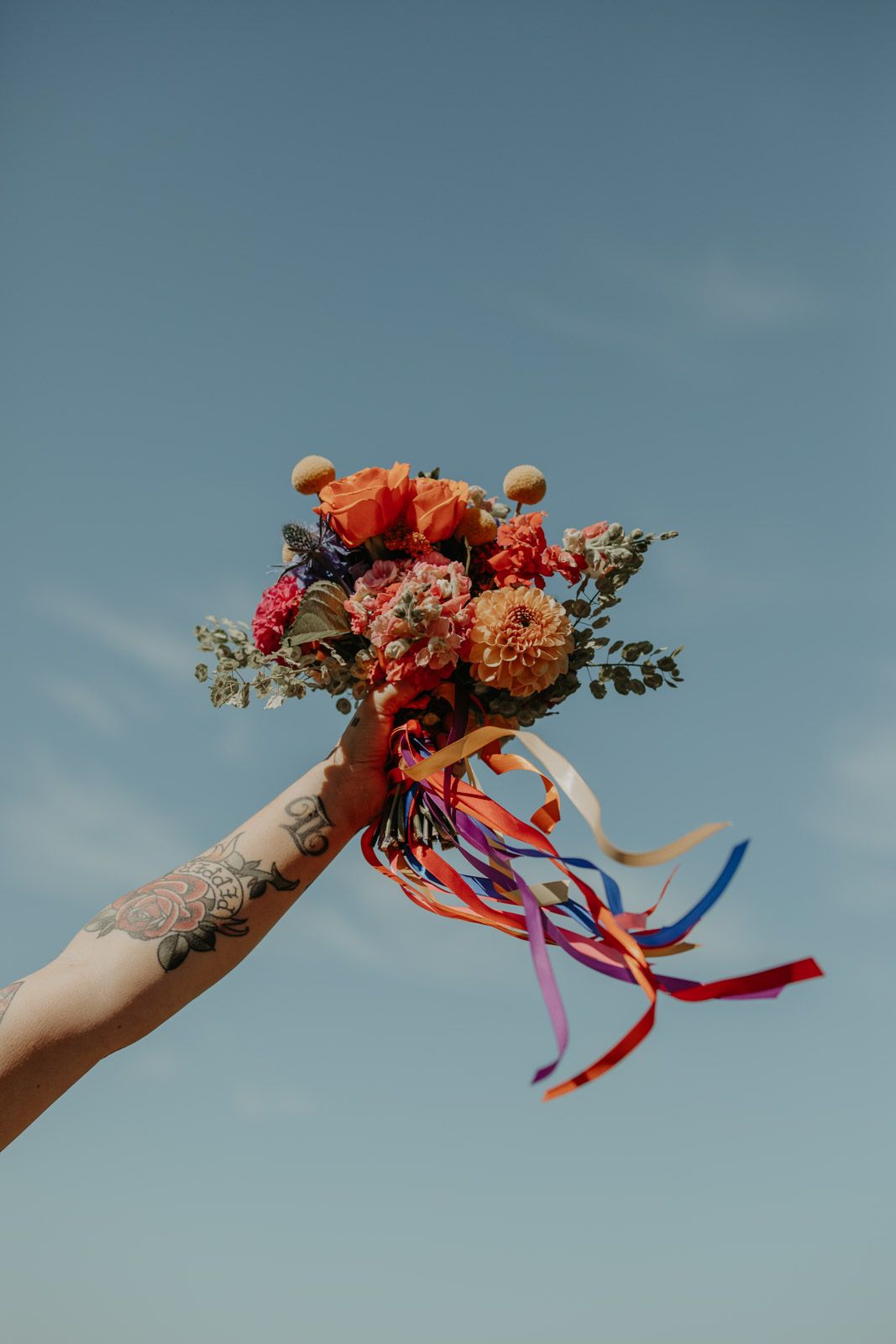 Colorful floral bouquets with streaming ribbons held up against a bright blue sky.