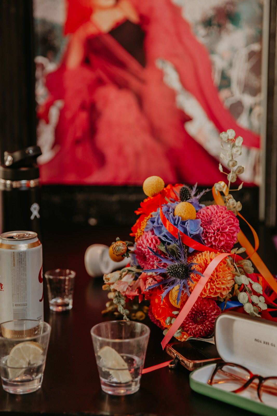 Colorful floral arrangements with bright red and blue blooms sit alongside glass tumblers on a dark wooden table.