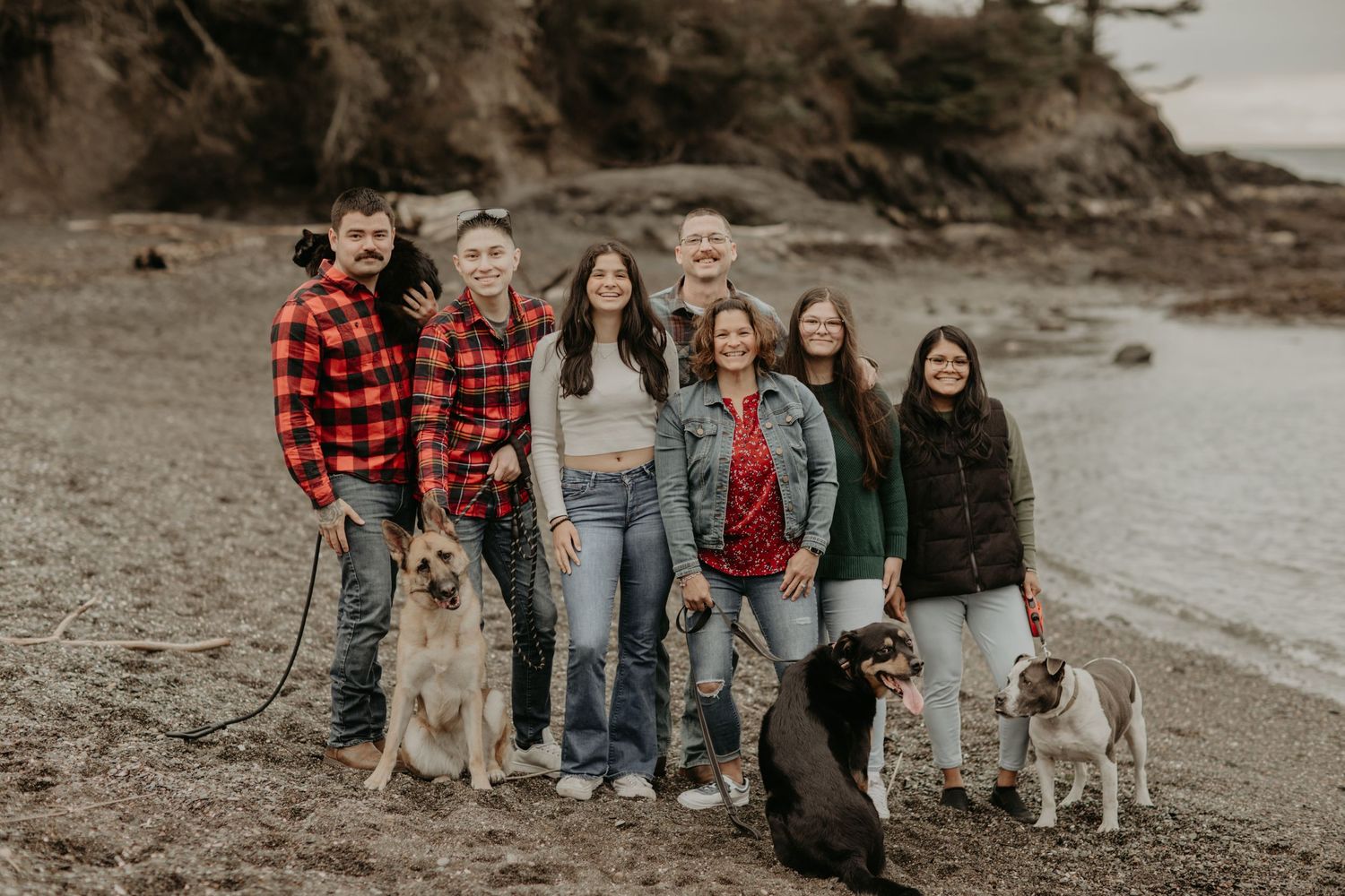 A group stands together with their dogs on a rocky beach on an overcast day.