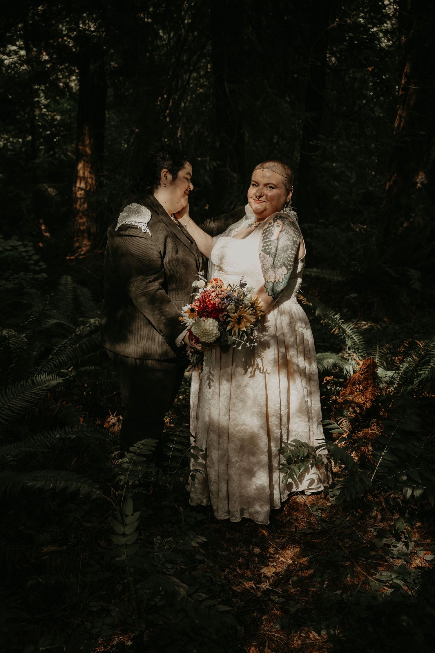A romantic wedding couple embraces in a moody forest setting with dramatic lighting and autumn colors.