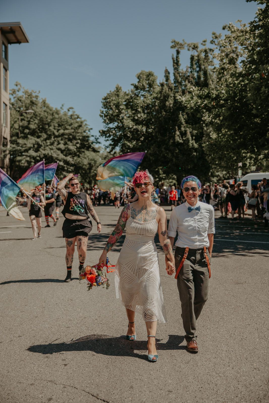 A group of people walking together at an outdoor event with rainbow pride flags waving in the sunlight.