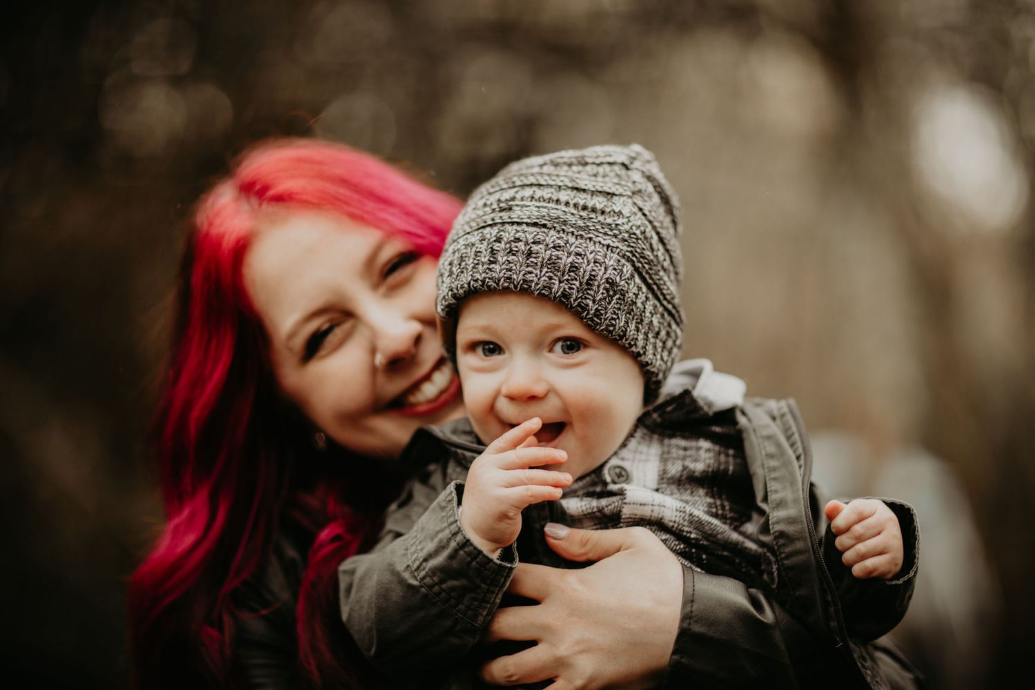 Two people share a joyful moment outdoors, with vibrant red hair contrasting against a blurred natural background.