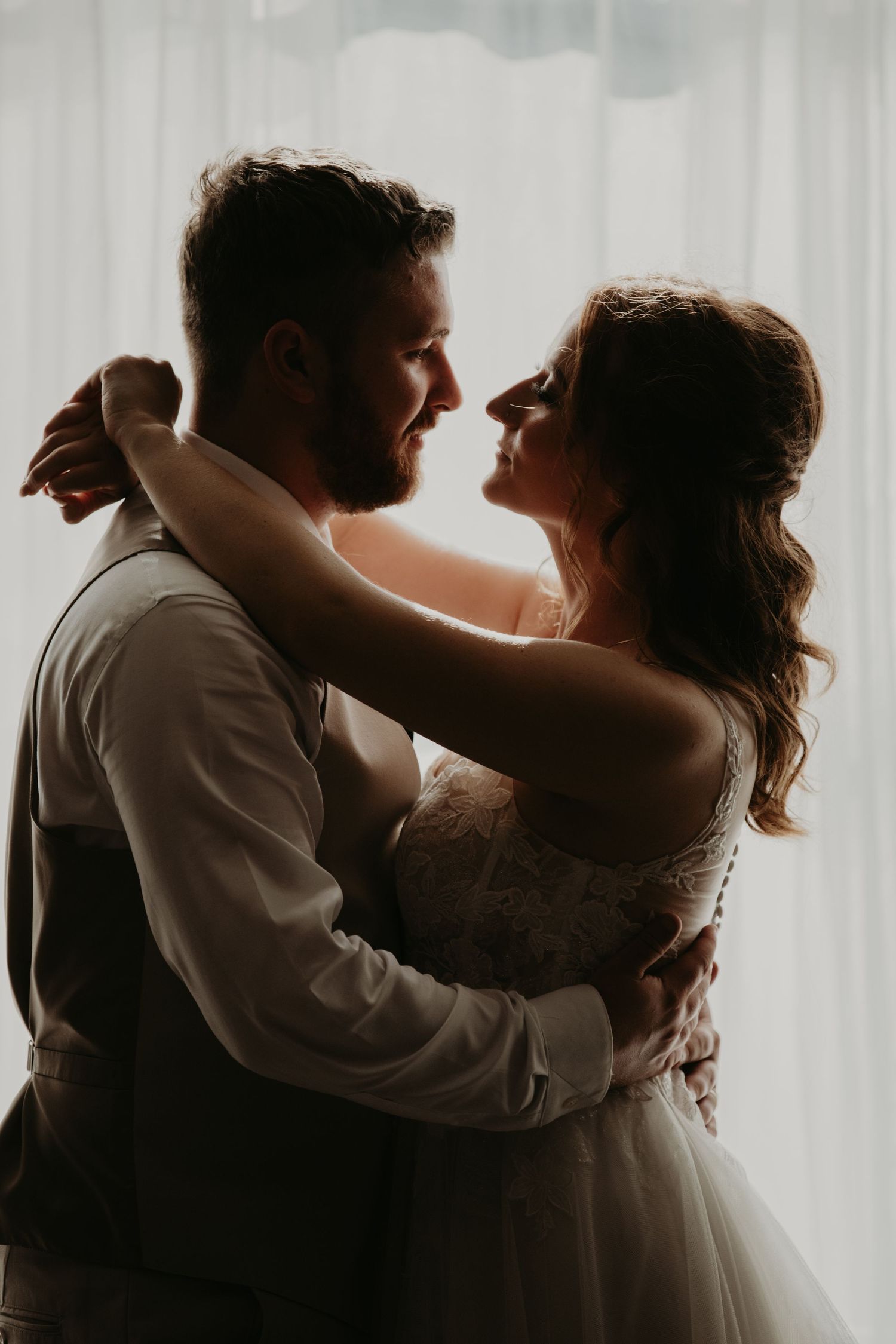 Romantic backlit wedding portrait with soft white curtains.