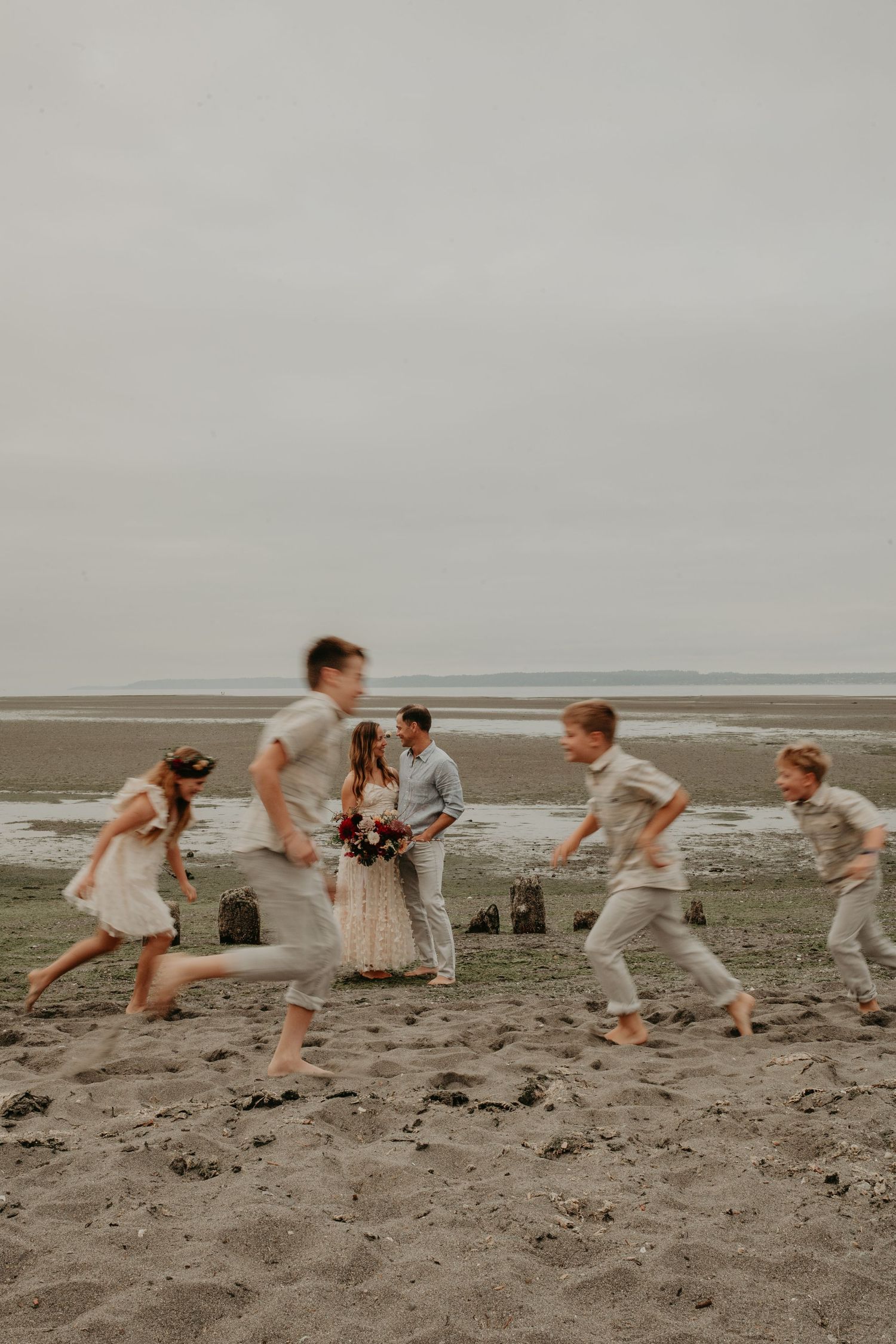 A group plays and runs together on a misty beach with overcast skies in the background.