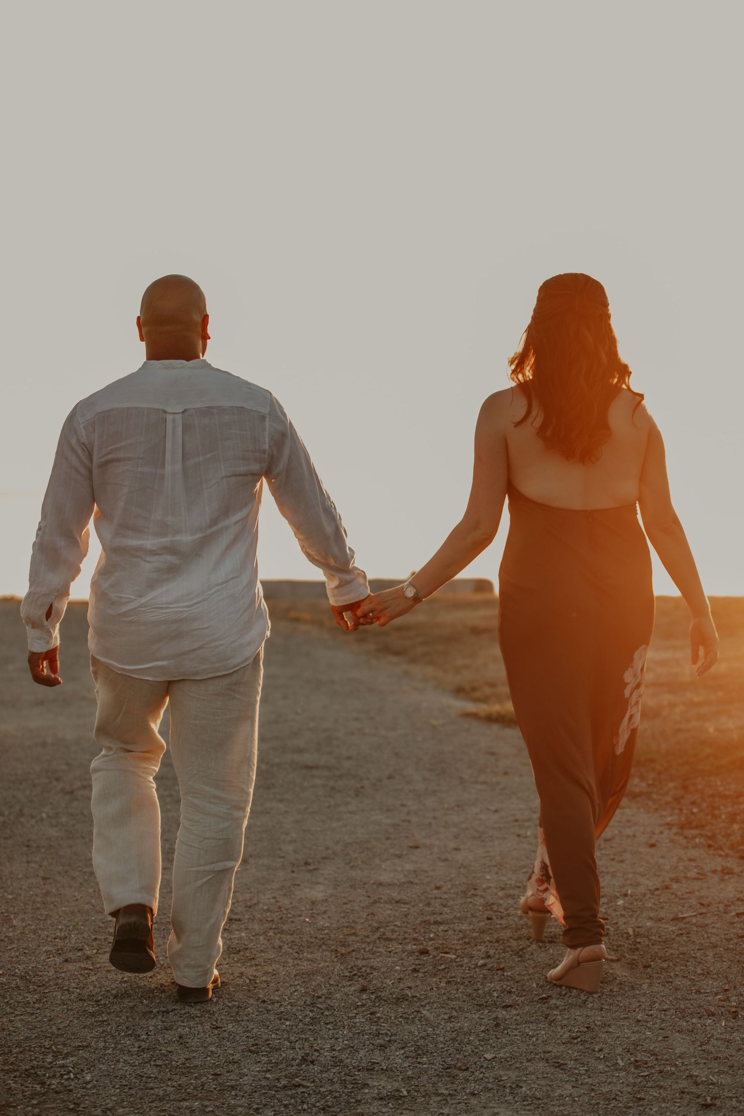 Two people walking uphill together during golden sunset, shown from behind in silhouette.