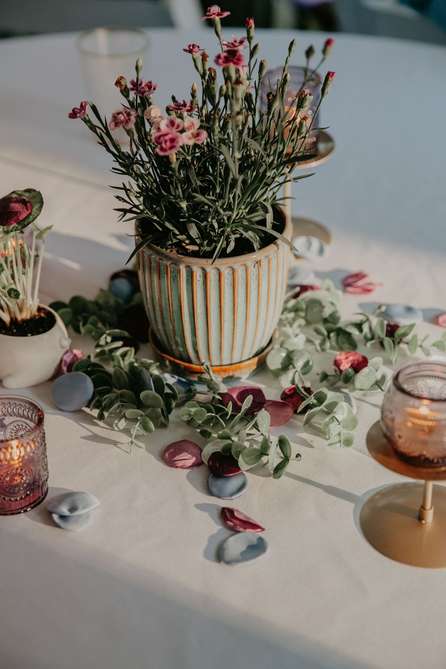 Elegant table decor with potted flowers and candles in striped vases along a white tablecloth.