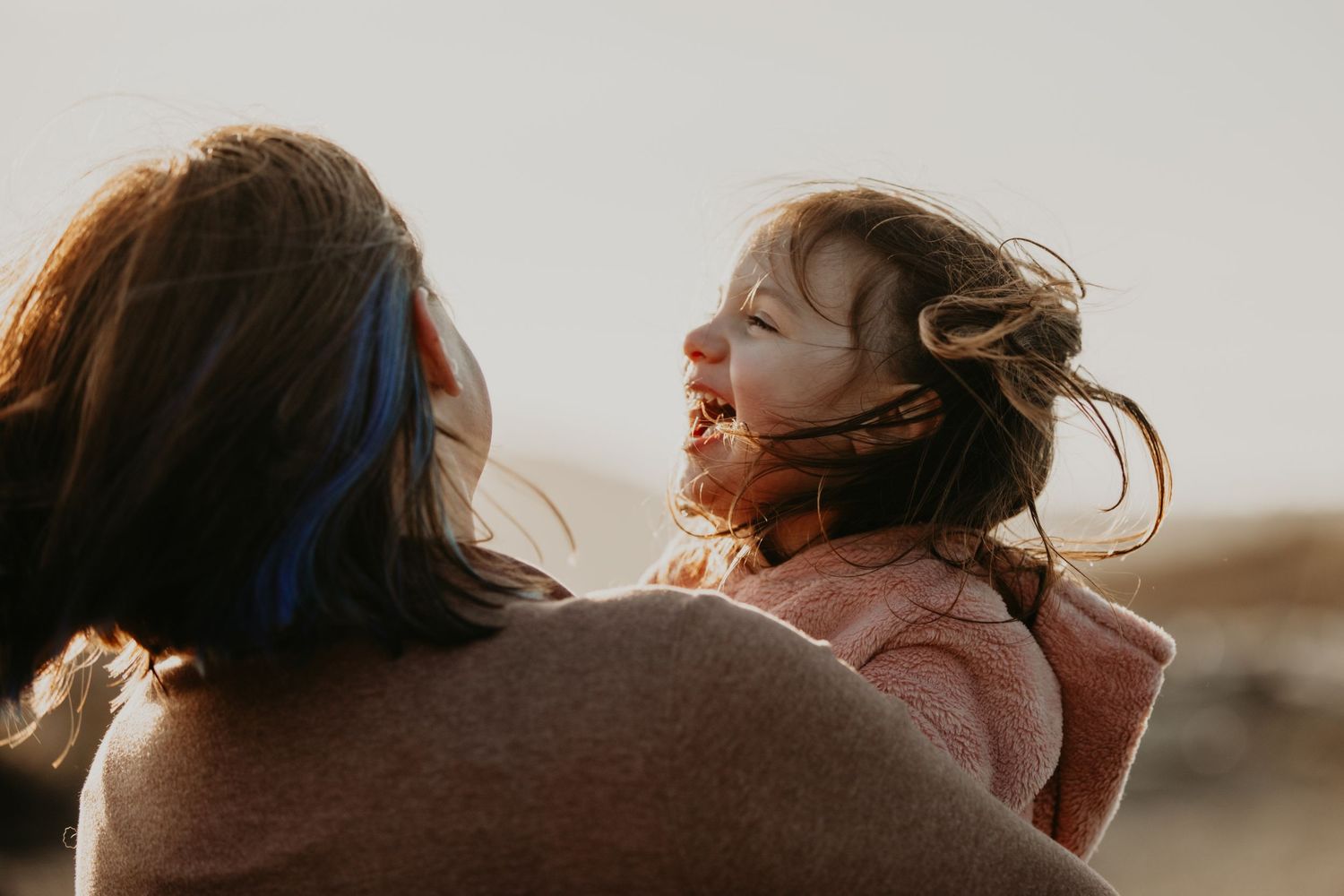 Two people share a tender moment outdoors at sunset while their hair blows in the wind.