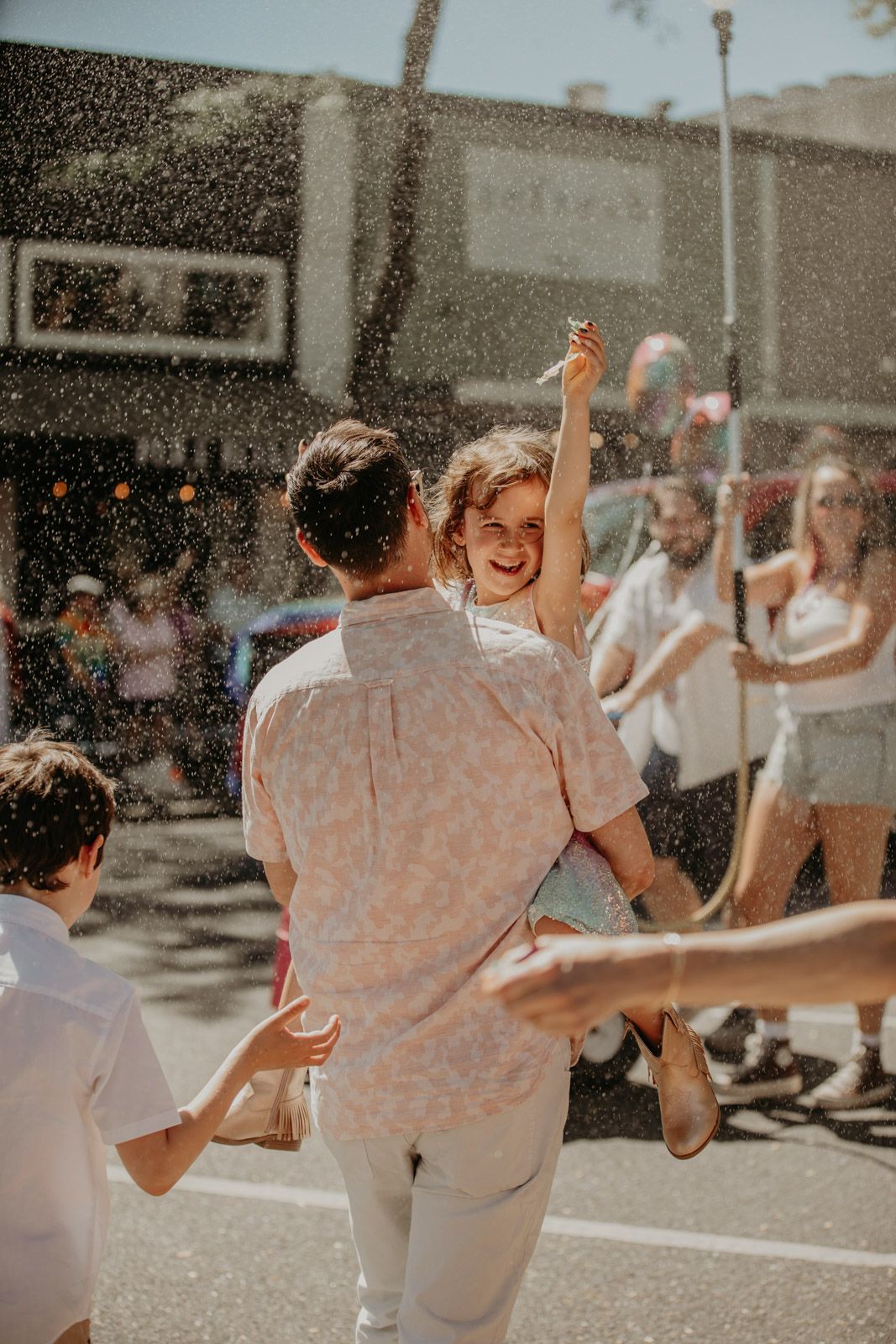 A couple dances joyfully in the sunlight while water sprays around them on a summer day.
