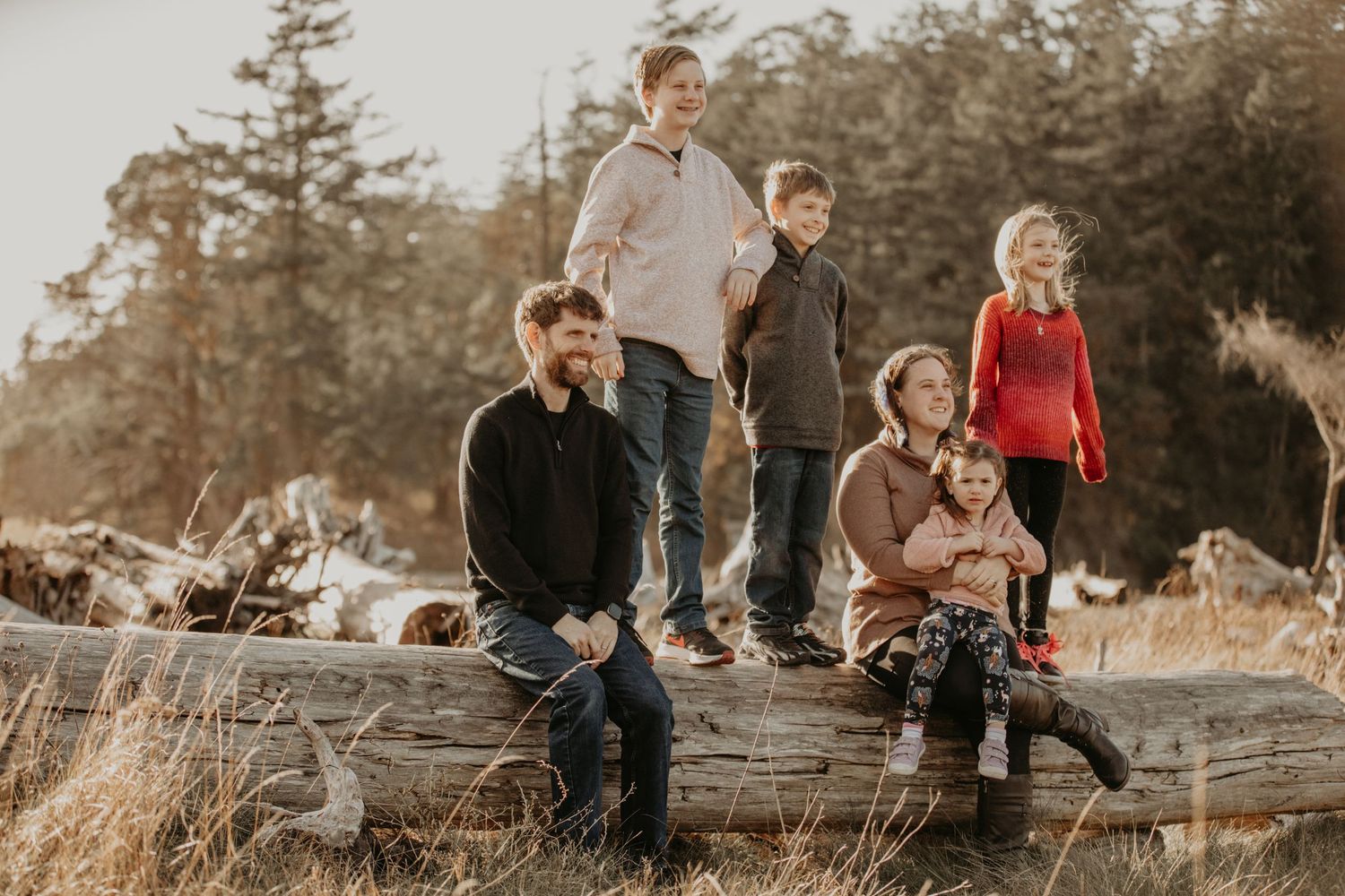 A group poses together on a fallen log at sunset in a natural outdoor setting.
