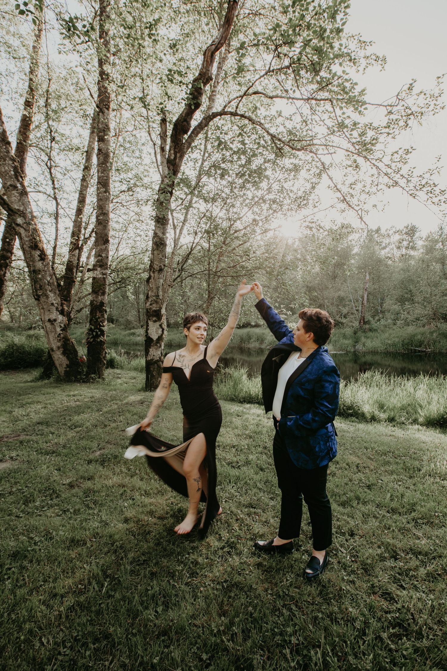 Two people dance together on a grassy lawn surrounded by tall birch trees in ethereal moody lighting.